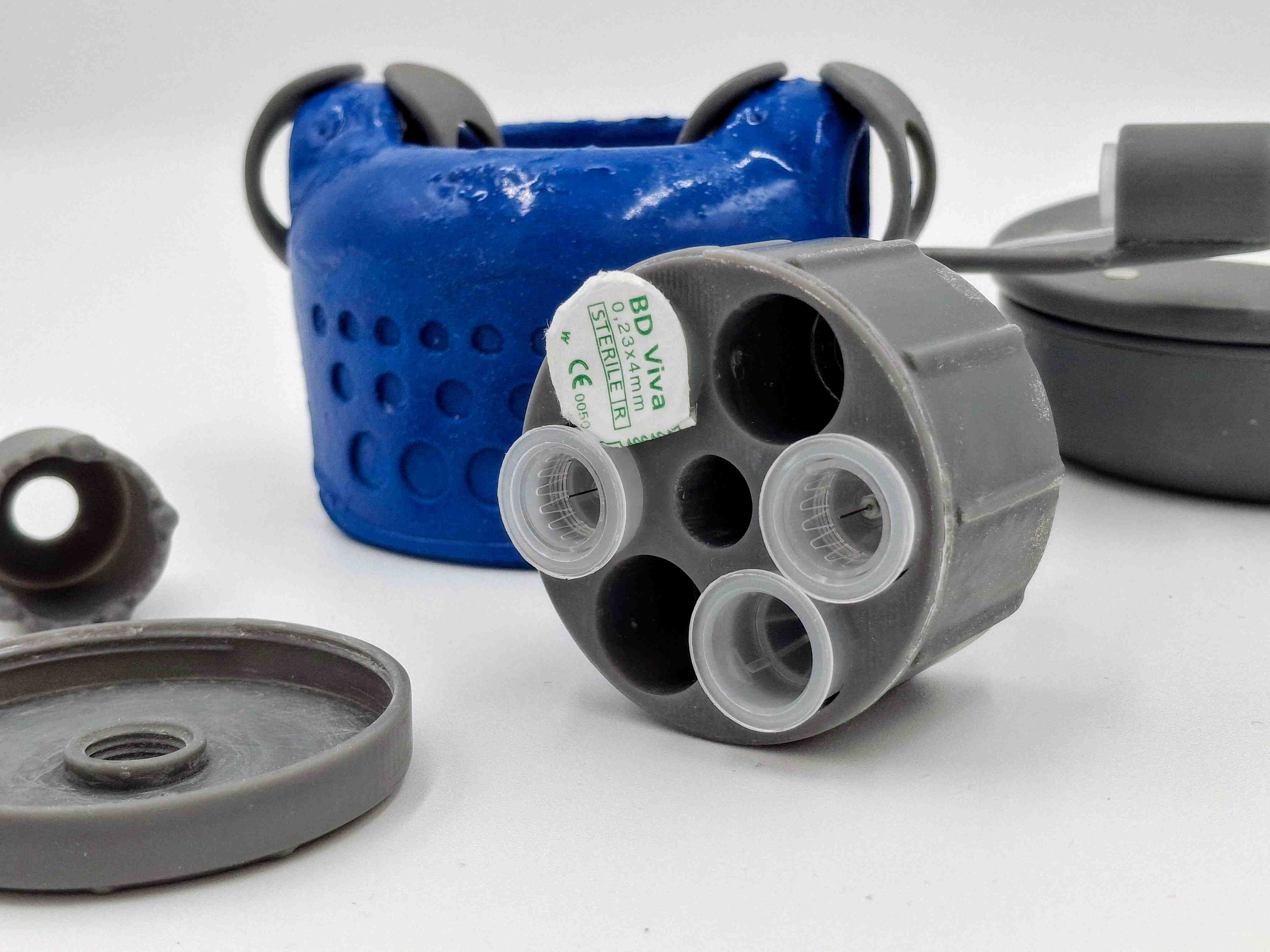 Hylow Injector zoomed in photo, seeing its circular blue form in the background whilst the needle storage is at the front showing needles stored inside.. The storage is at the center and the rest of the components are around it.