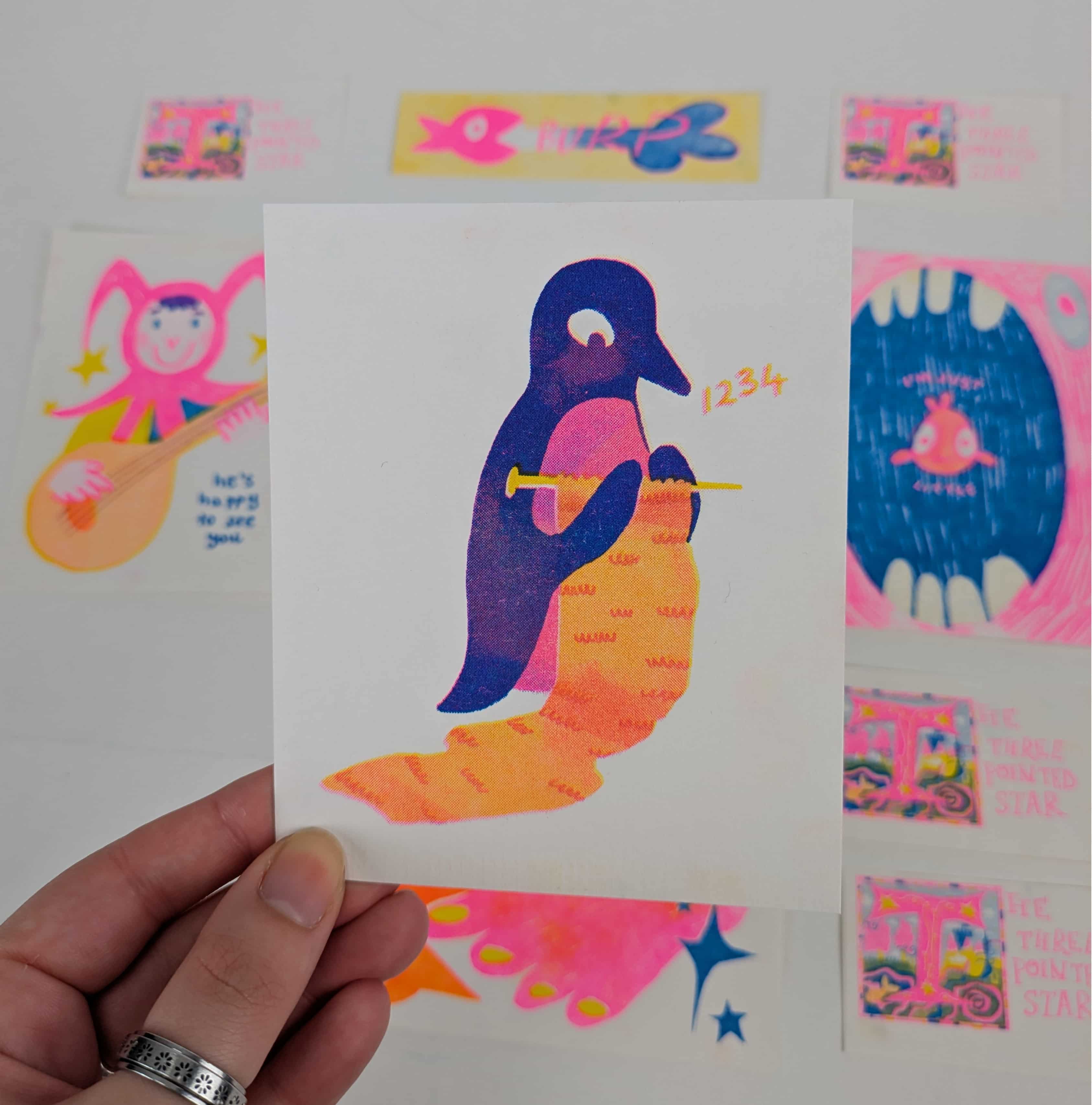 A risograph printed postcard with a purple penguin knitting an orange scarf.