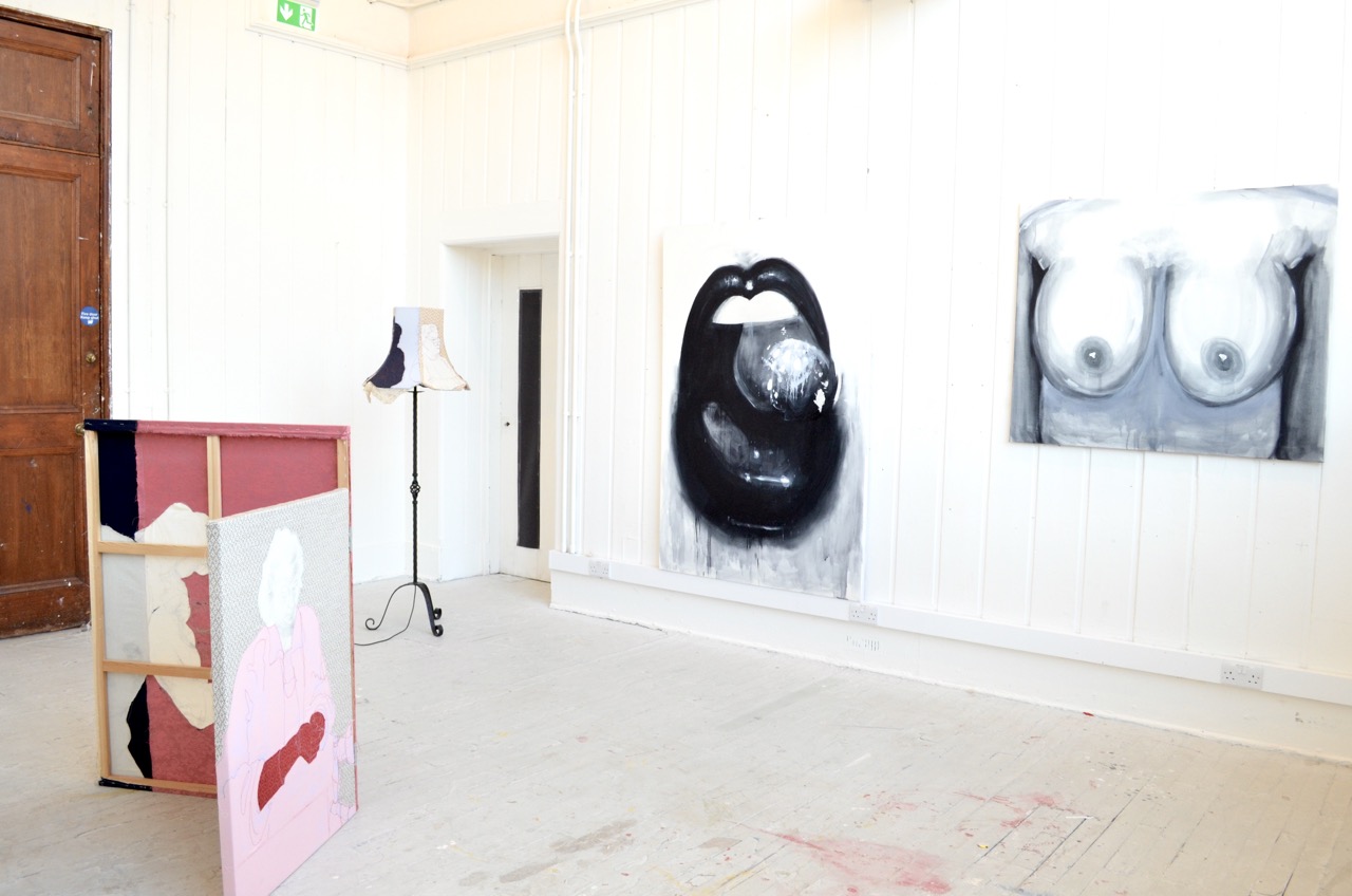 Big mouth and boobs painting in black and white alongside a fabric screen and lamp by another artist