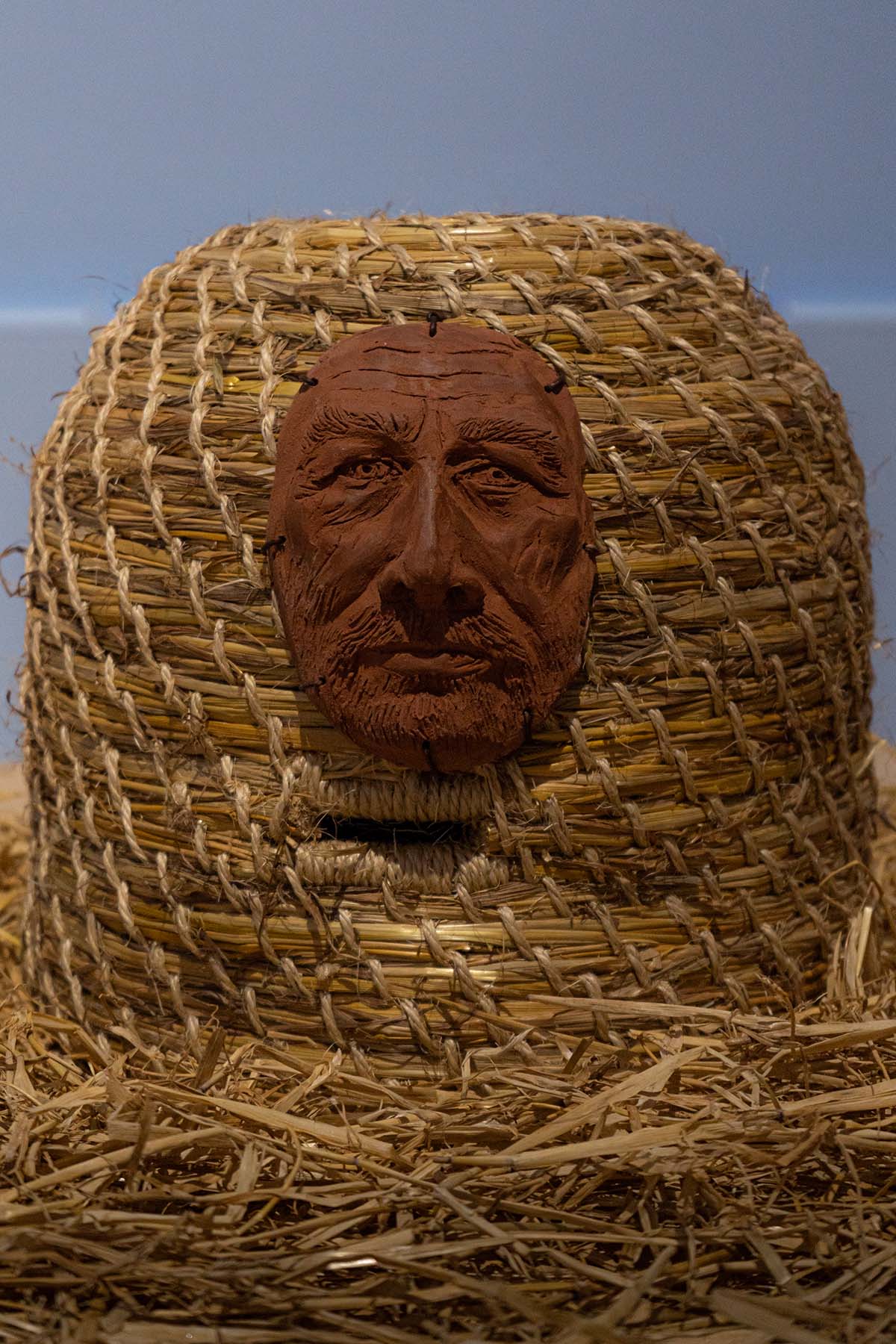 A Bee Hive/Skep, with a ceramic terracotta male portrait attached to the front, using leather thread.