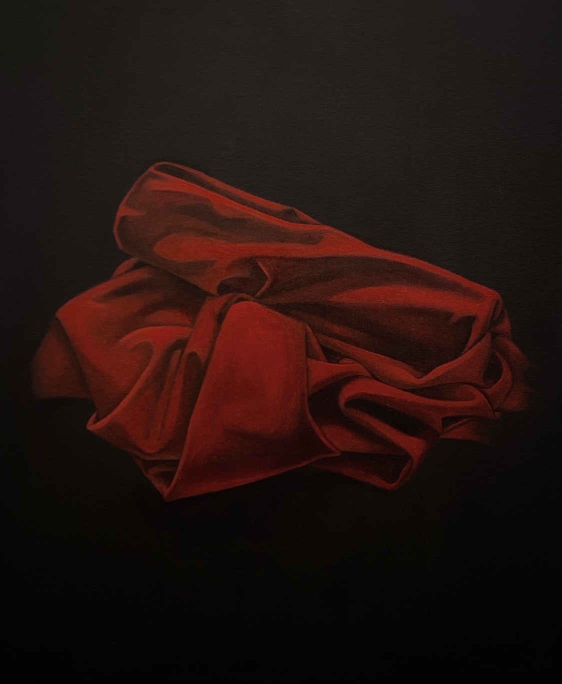 Painting of red fabric positioned at the center of a black void.