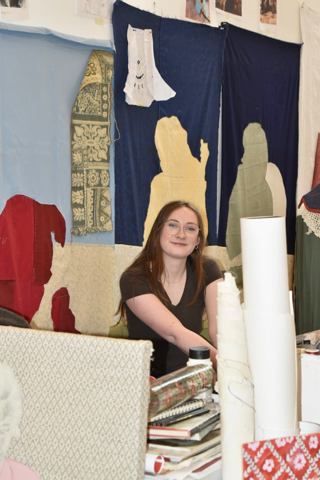 Woman sitting in a studio space surrounded by fabric. 