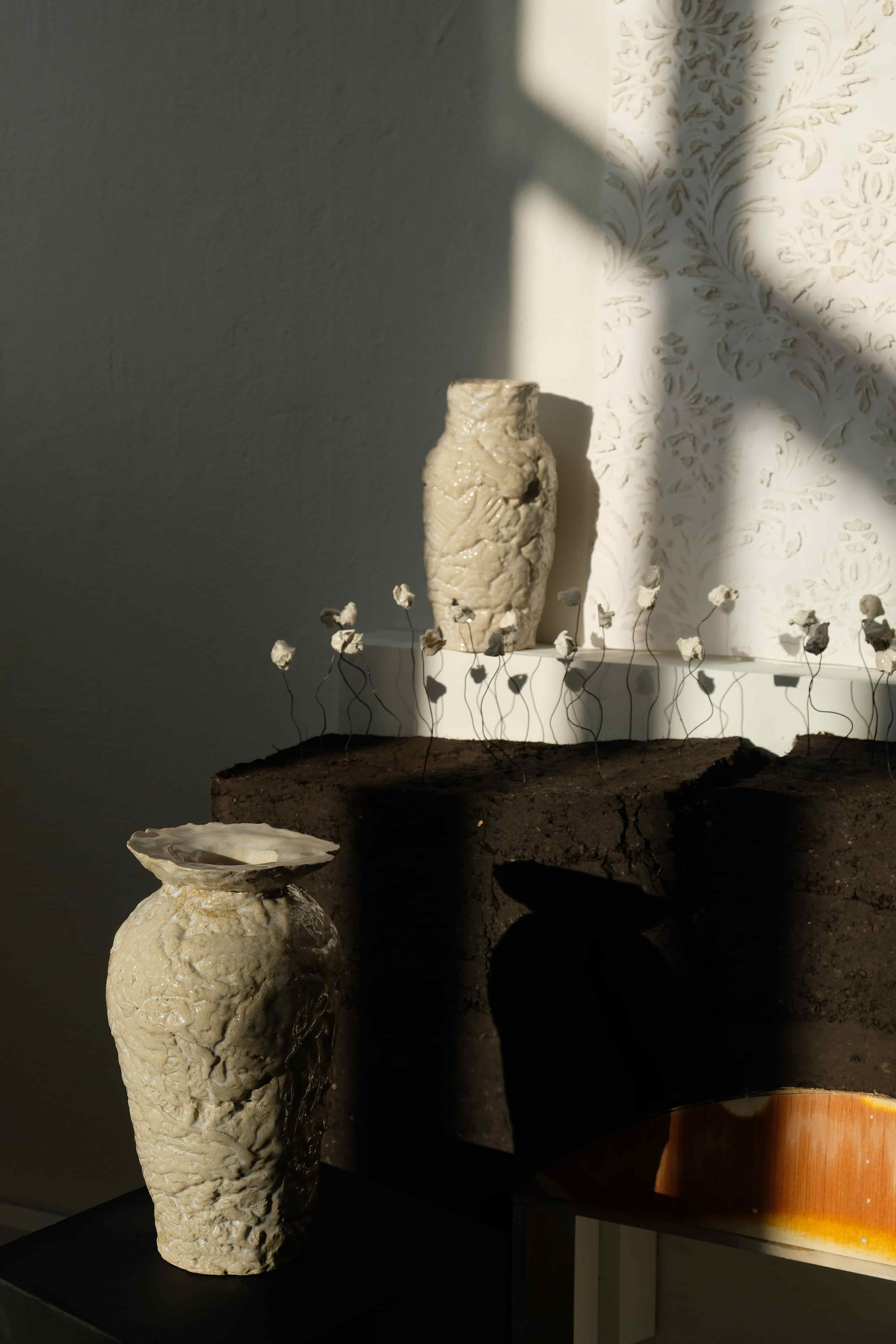 Two ceramic vases on top of a plinth and earth rammed sculpture.