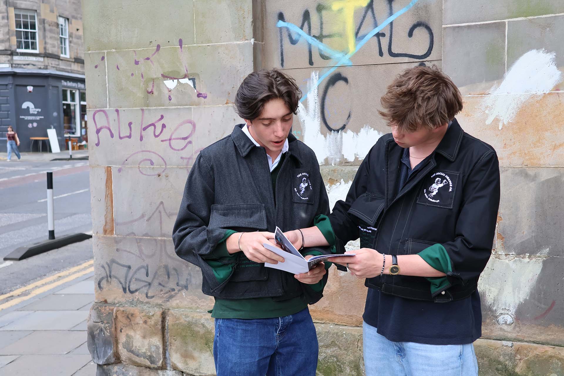 Two people reading monthly magazine on street corner