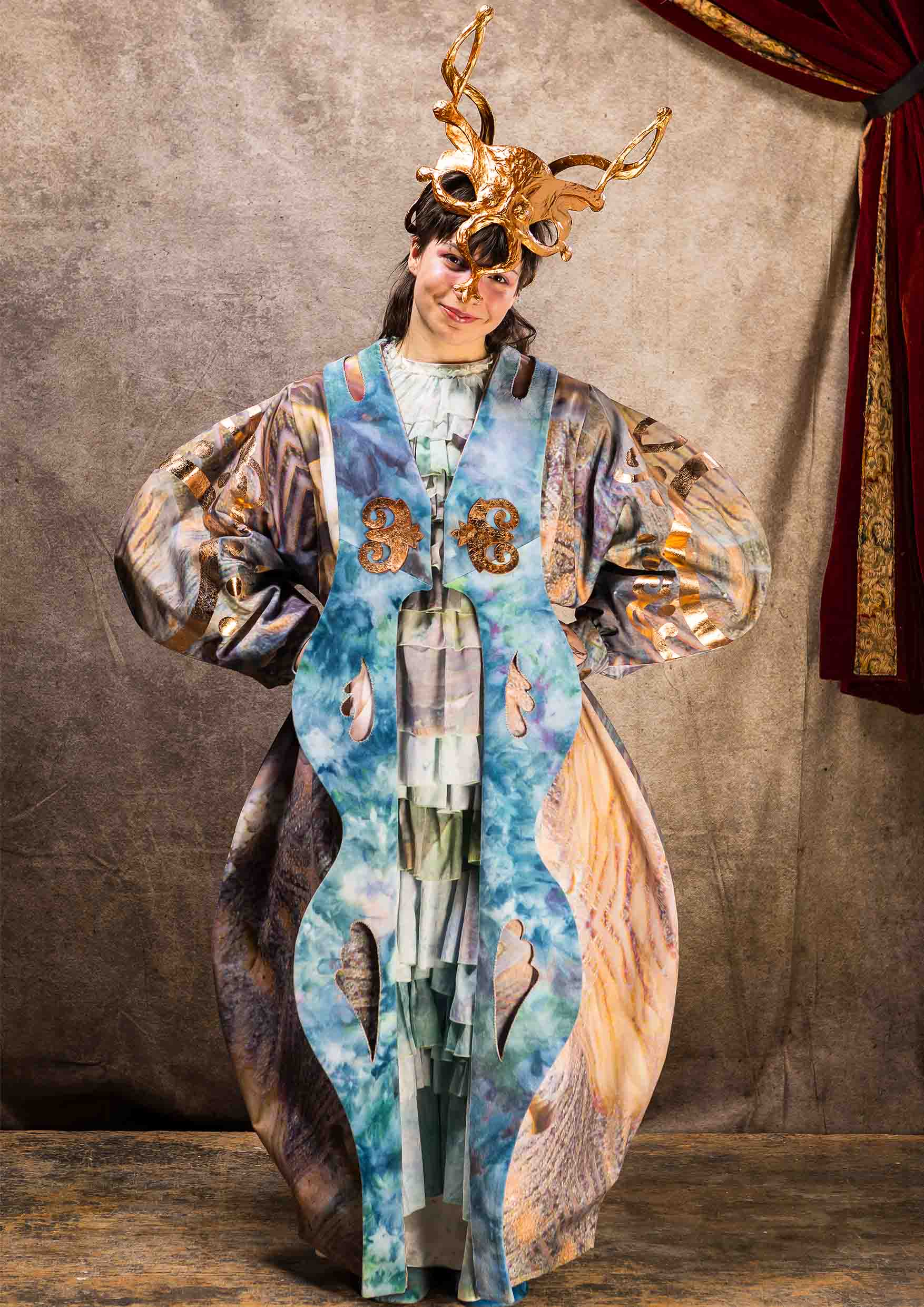 A performer with hands on hips wearing a long coat and metallic headpiece