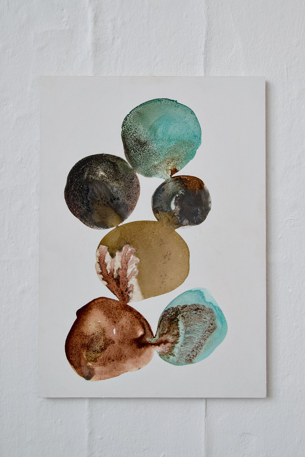 A 30 × 40 cm portrait-format canvas made with natural inks. On a white background, seven rounded pools of colour form a loose vertical chain down the centre of the canvas. The colours include turquoise blue, dark grey-black, ochre brown, rust orange, muted green, and pale blue-green. The pools touch and bleed into one another in places, with visible sedimentation, speckled crystallised edges, translucent staining, and darker concentrated patches of pigment.