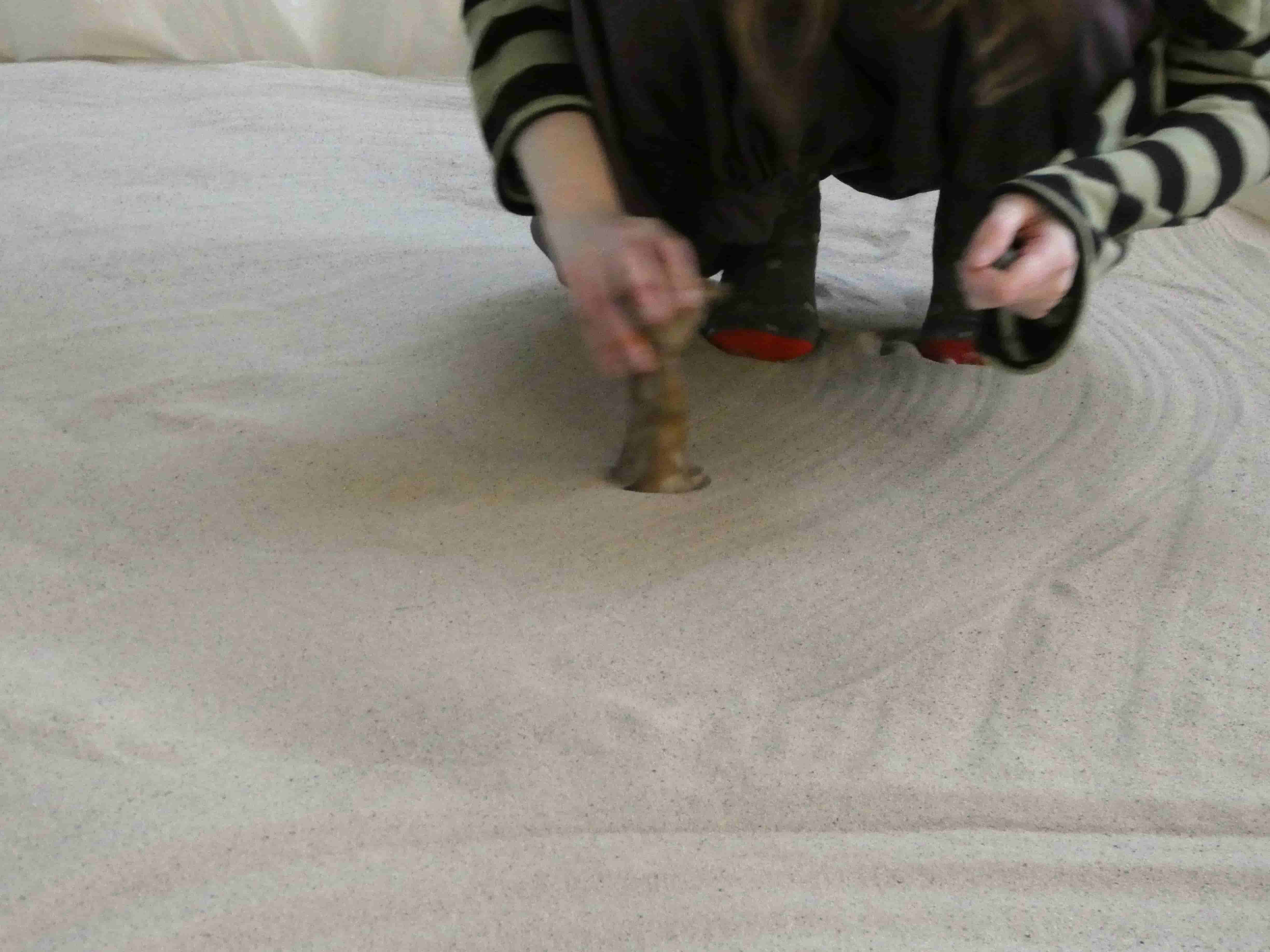 Someone crouching in sand, placing a ceramic sculpture 