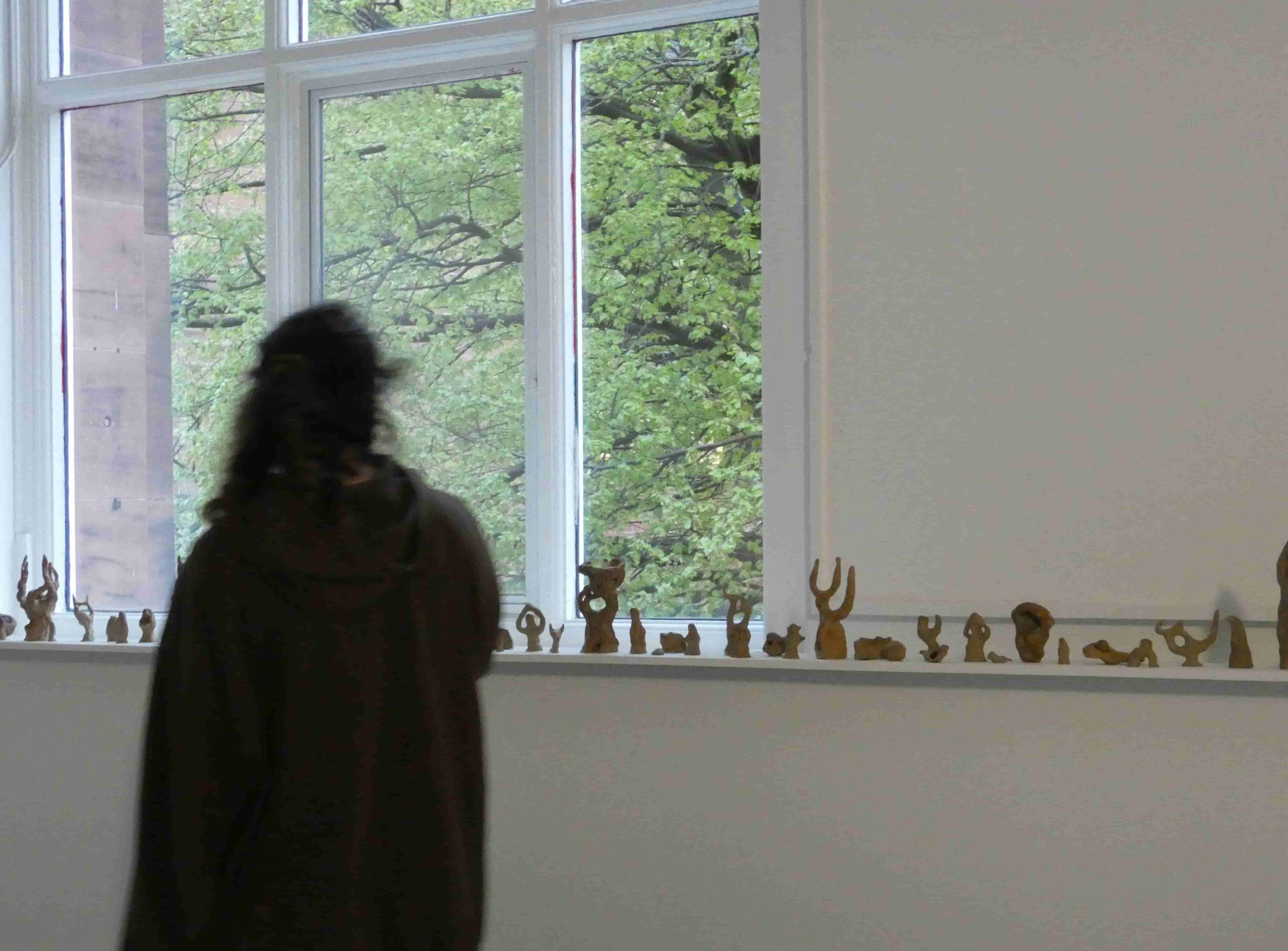 A silhouetted figure walking past a shelf of ceramic sculptures, in front of a window