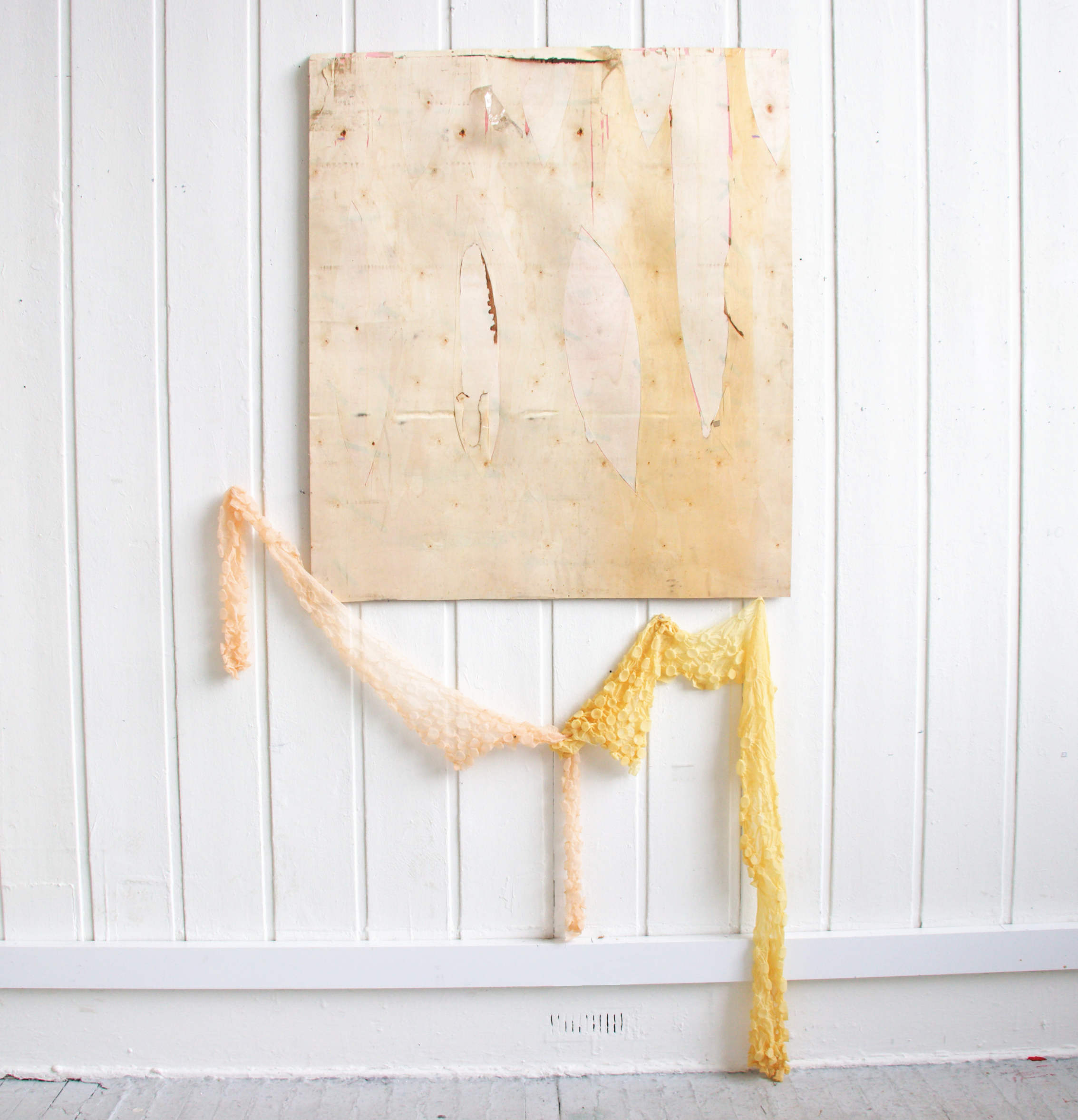 Square, distressed wooden board, underneath which is draped and steamed  pink and yellow polyester fabric