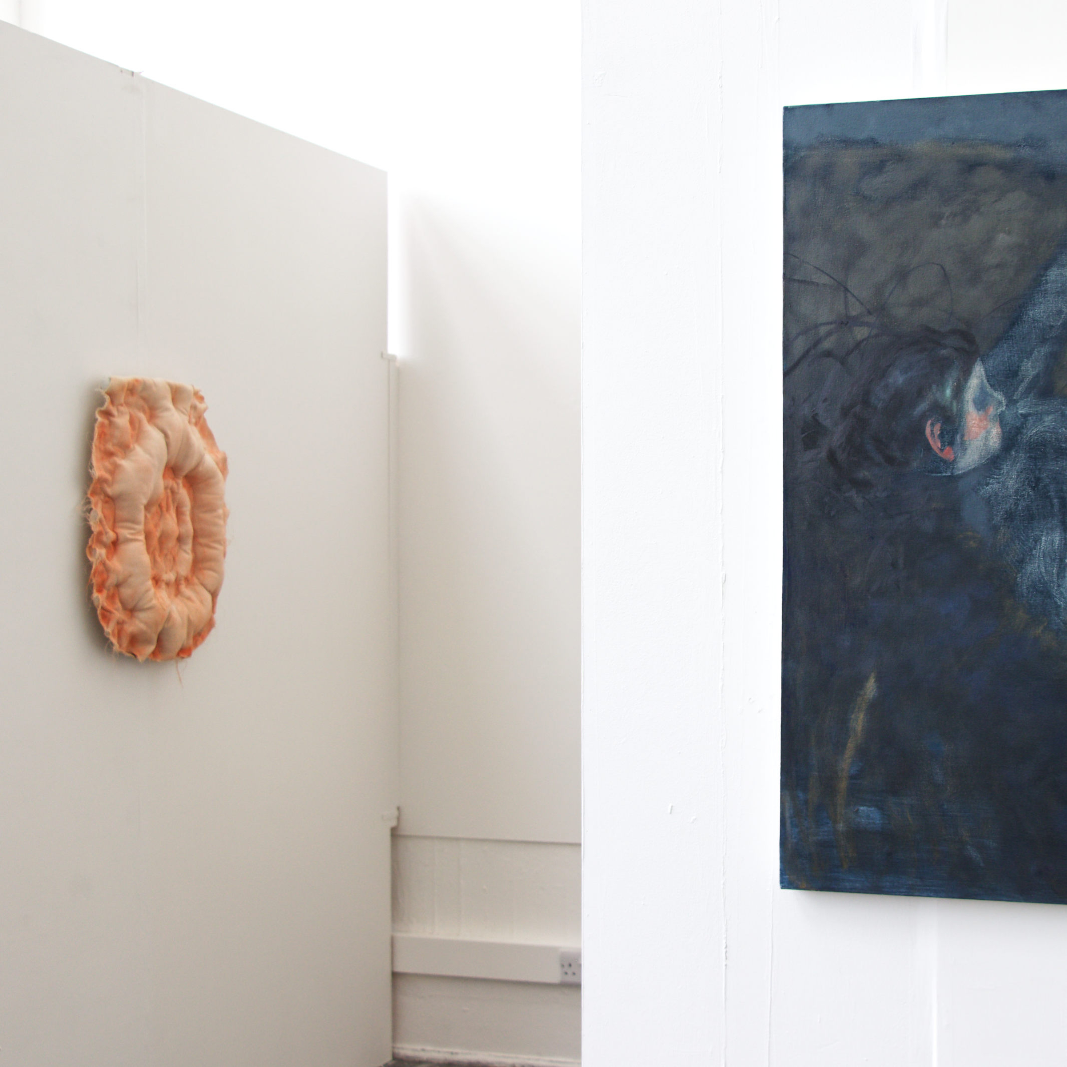 Red cushion mounted on the wall, parallel to a blue painting of a girl with a highlighted pink ear