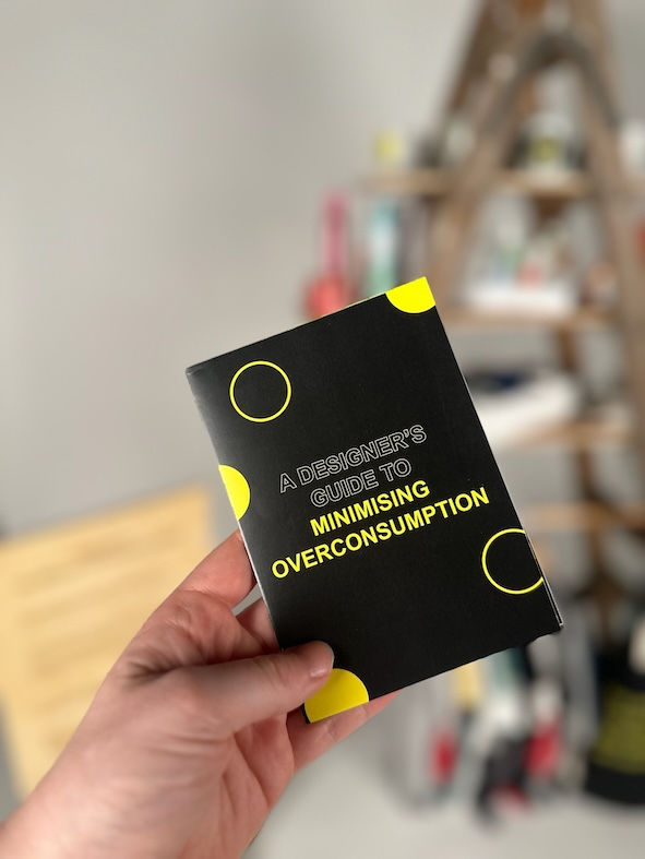 Zine held up in front of The Museum of Overconsumption