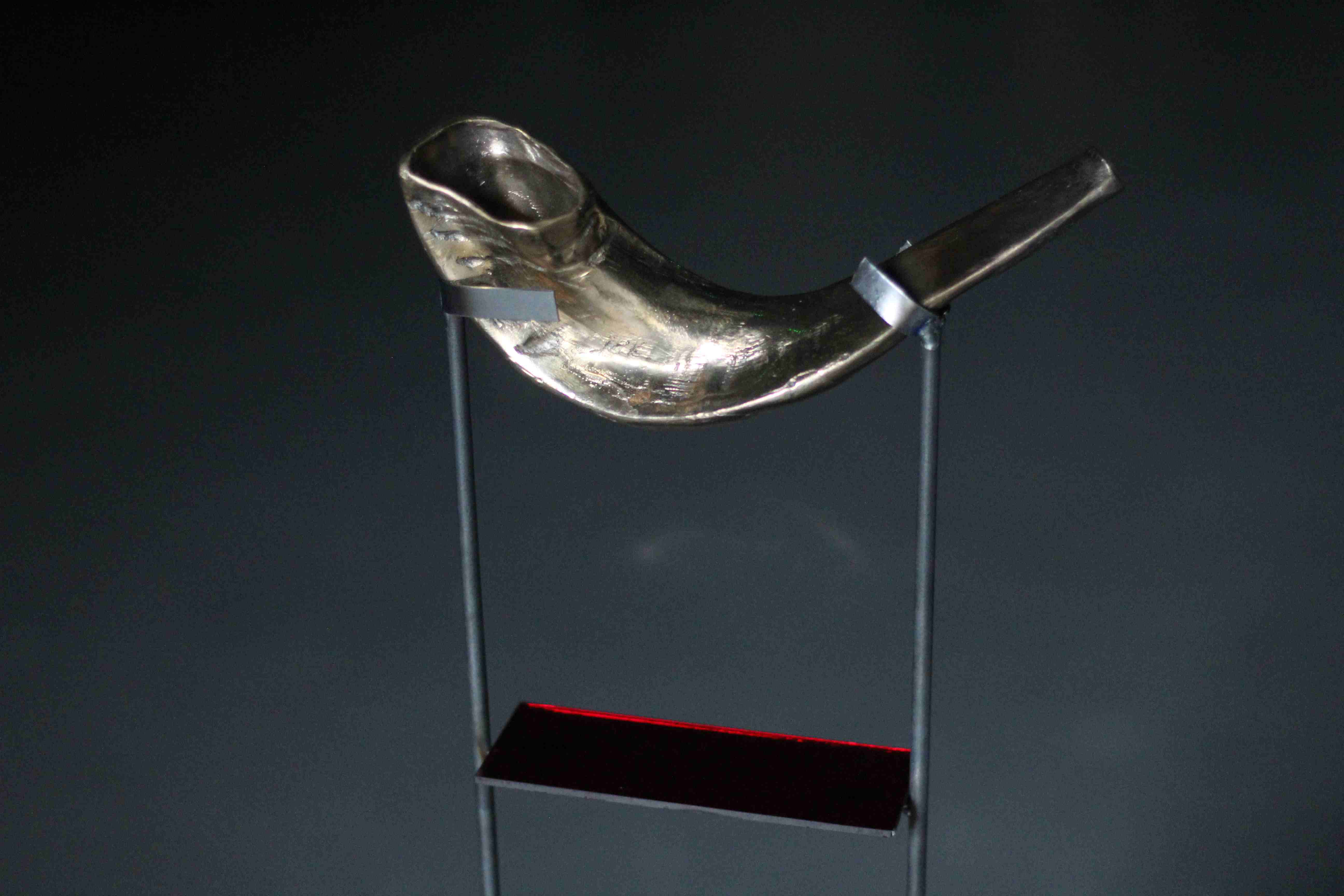Brass horn being suspended over a plane of red glass.