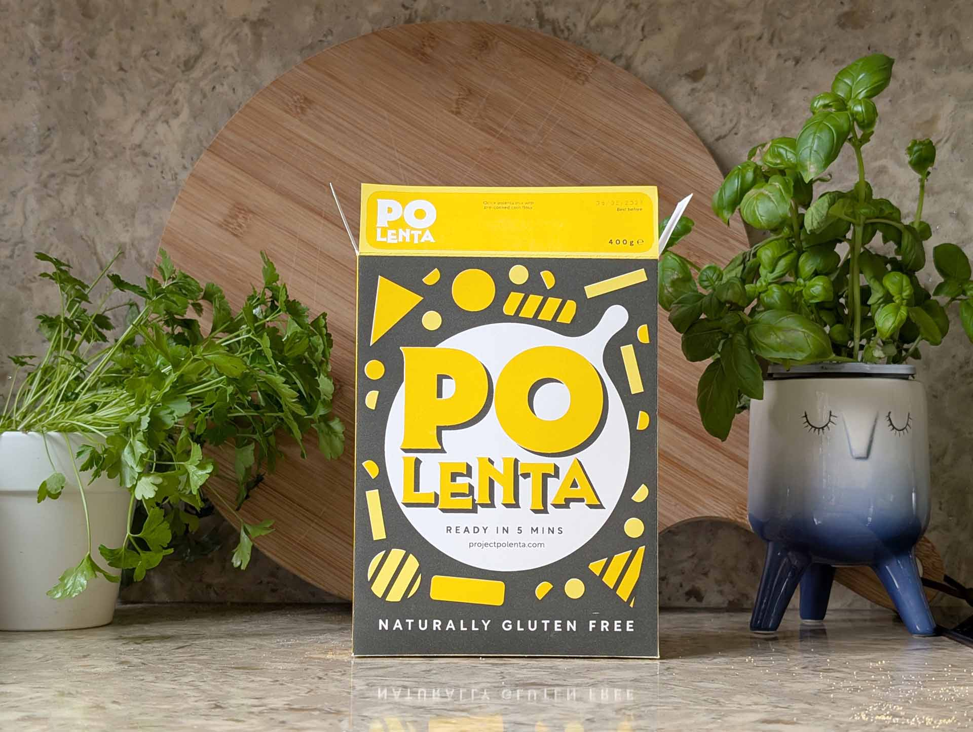 Polenta packging sitting upright on stone kitchen counter, with potted herbs on either side.