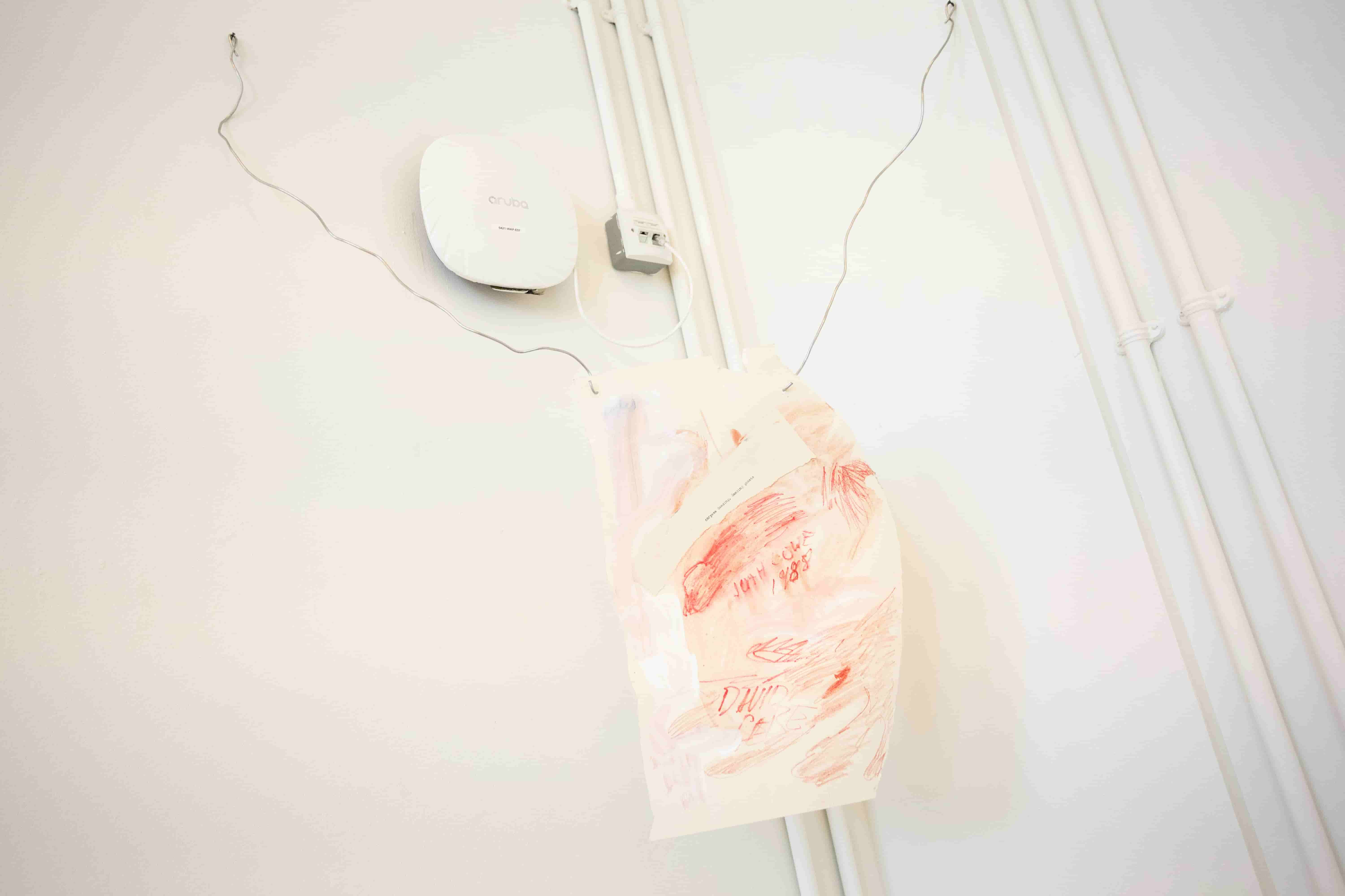 A piece of red and white paper reading 'Corpses Dancing, Dancing Ghosts' suspended by two lengths of wire in a corner