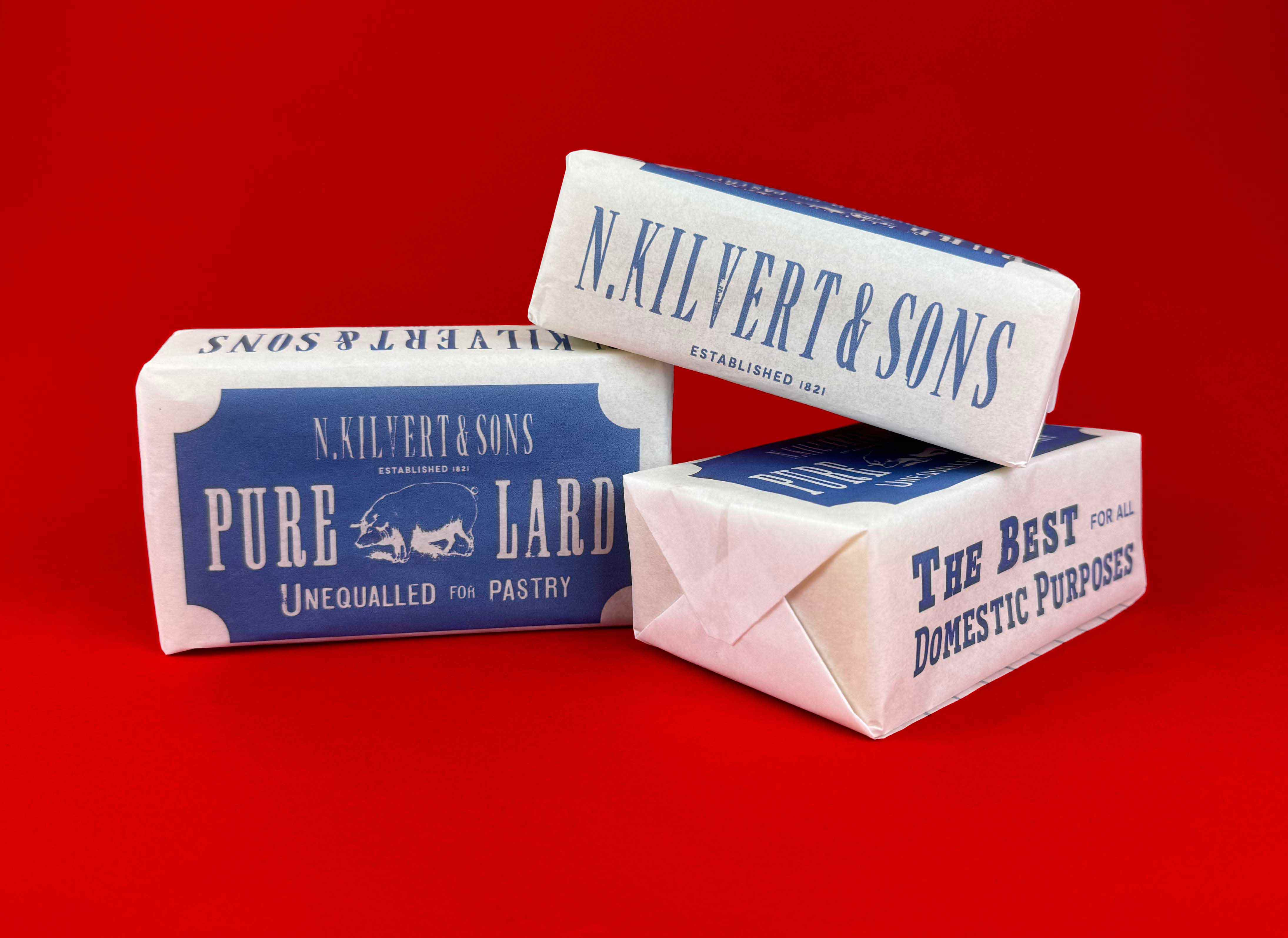 three identical lard products that have been placed on top of each other to display the various designs on each side of the packaging. They are photographed on a bright red backdrop 