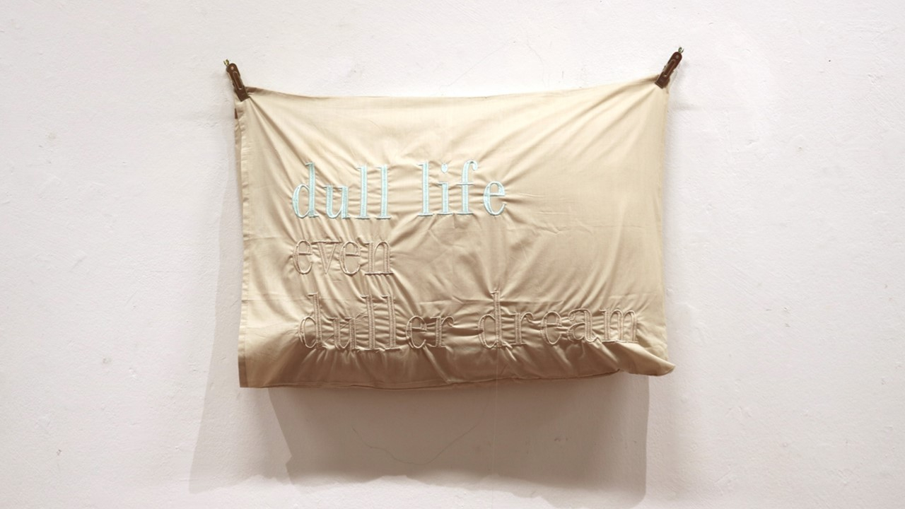 Beige pillow case with text written on it 'dull life even duller dream'