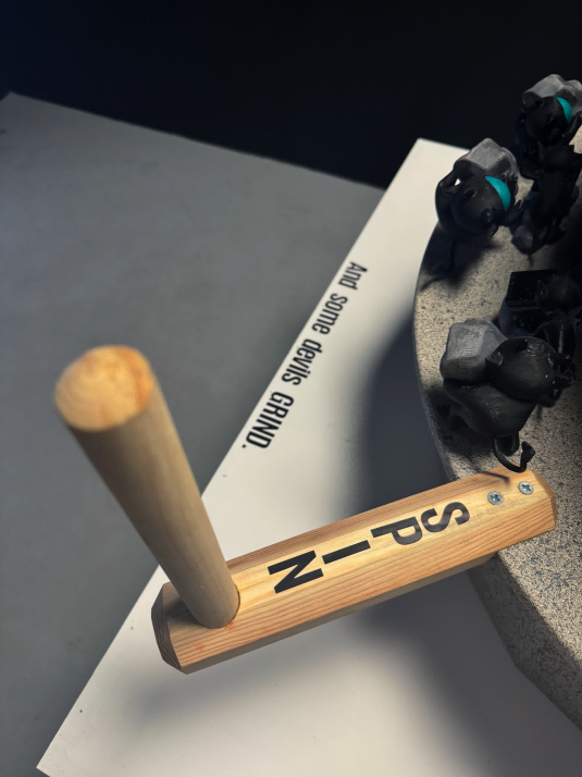 The plinth reads: “And some devils GRIND,” inviting viewers to interact by turning the crank attached to the bottom layer.