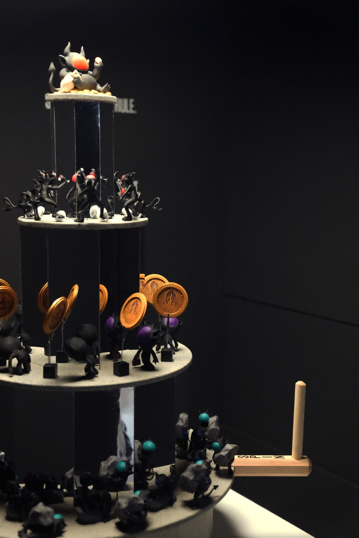 A tiered praxinoscope-inspired sculptural installation stands at the center of a dark exhibition space, viewed through an open doorway. The rotating tower features layers of silhouetted devil figures engaged in labor, echoing themes of capitalist hierarchy. On the black walls behind, white text reads “Some Devils” in repeated lines, reinforcing the work’s title and critical message.