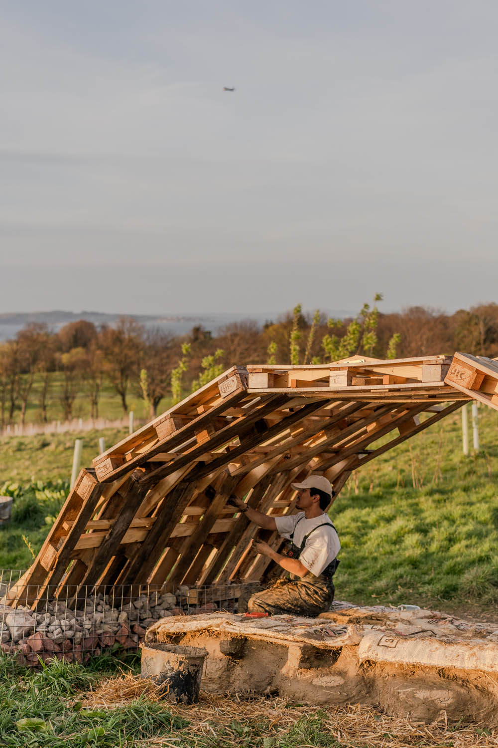 A man is seen working on the pallet arches, a plane is flying low in the background