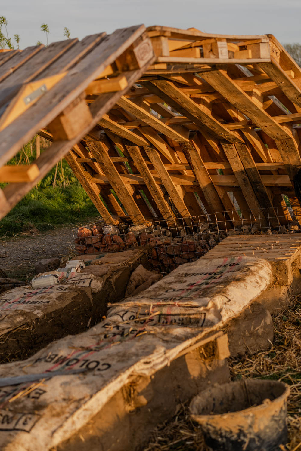 Photo of the pavilion covered with arched roof made of three rows of pallets covering two rows of benches; time of the day is sunsey