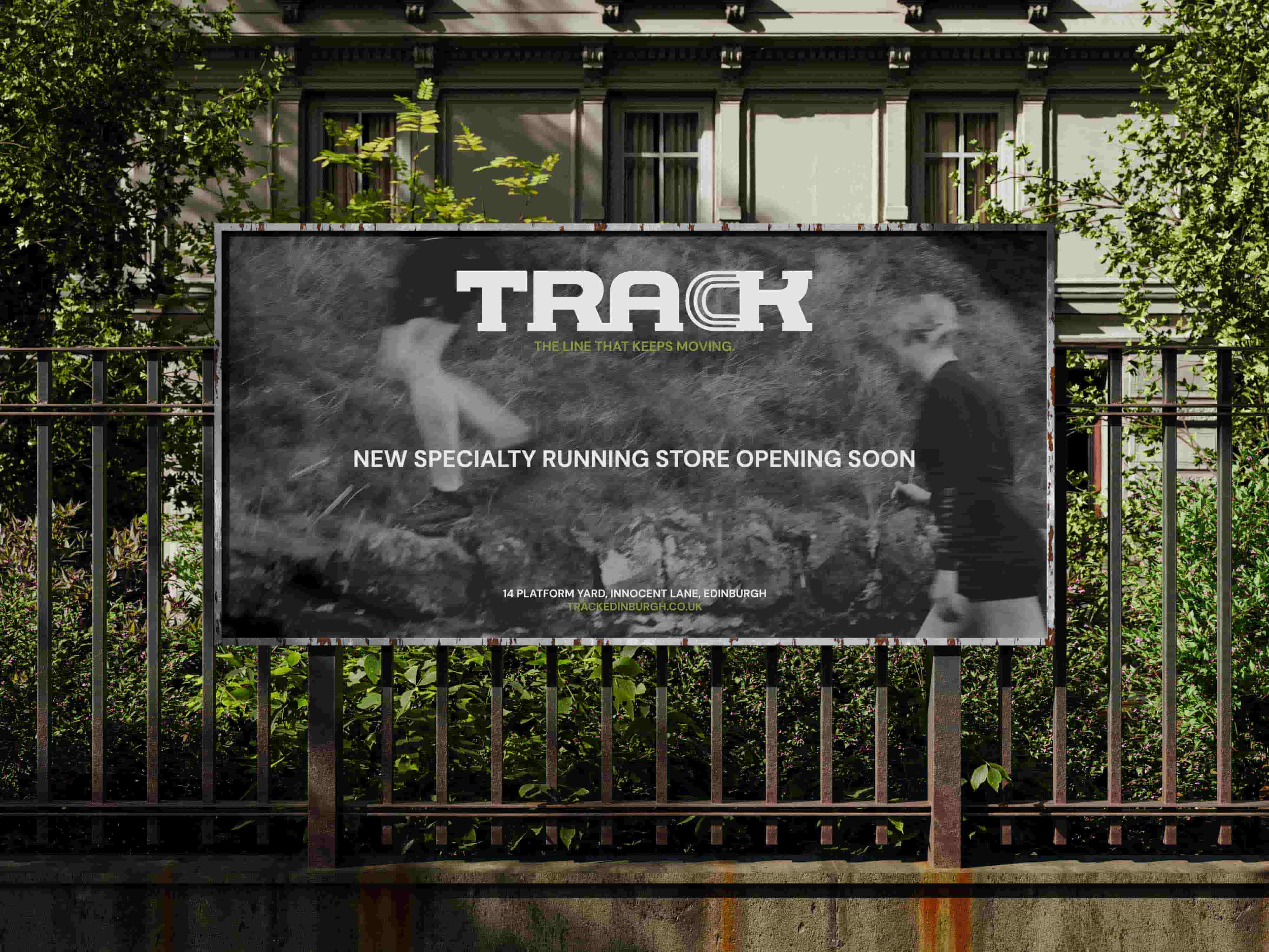     Large outdoor billboard for TRACK mounted against a metal fence in front of a residential building. The billboard features blurred black and white imagery of runners, the TRACK logo, and the text ‘New Specialty Running Store Opening Soon’ alongside the Edinburgh store address and website.