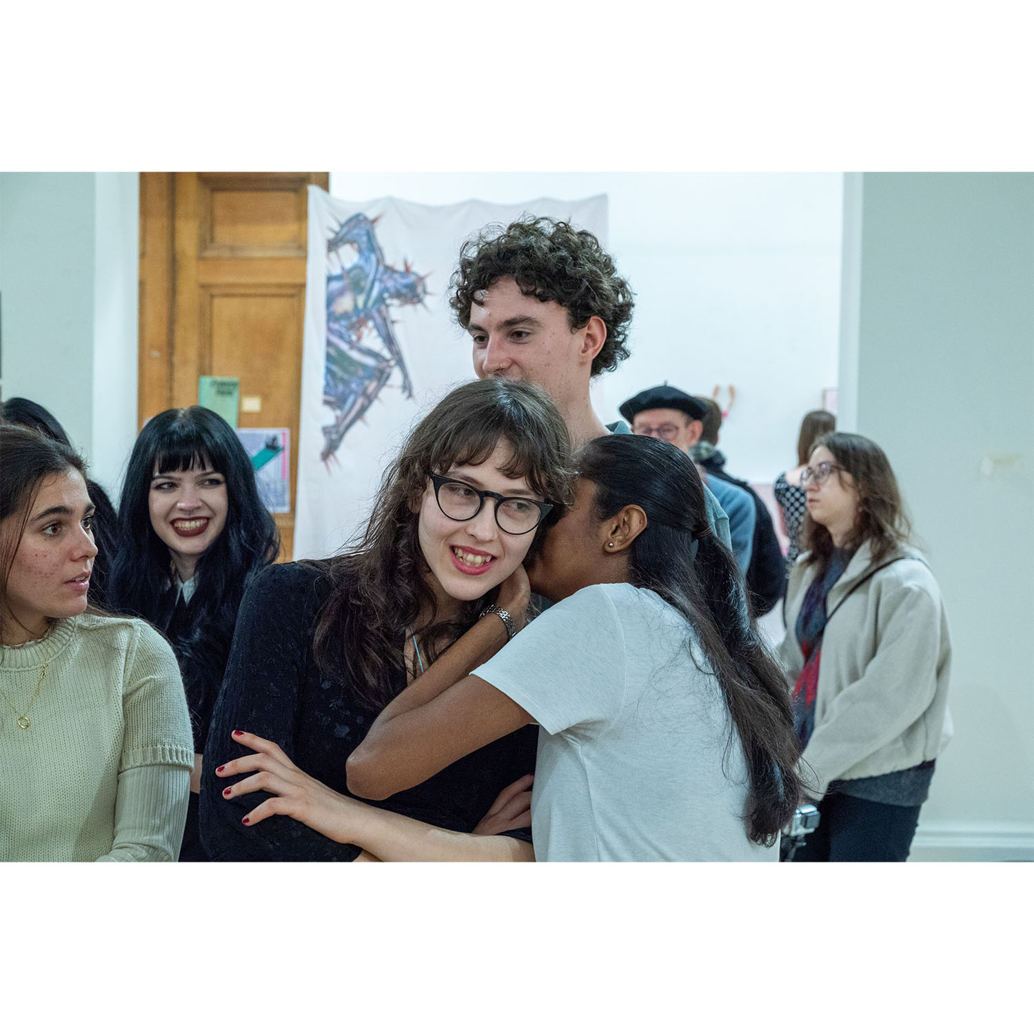 Performance artist whispering into an audience member’s ear while surrounded by viewers during the live performance.