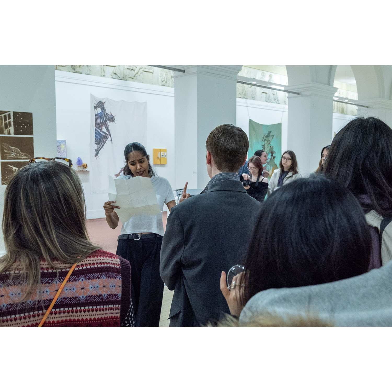  Live performance still of the artist reading aloud and gesturing toward audience members during the exhibition opening