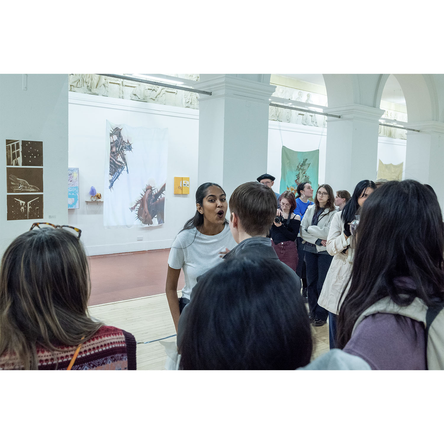     Performance artist reading from a folded sheet of paper while addressing an audience in a gallery space.
