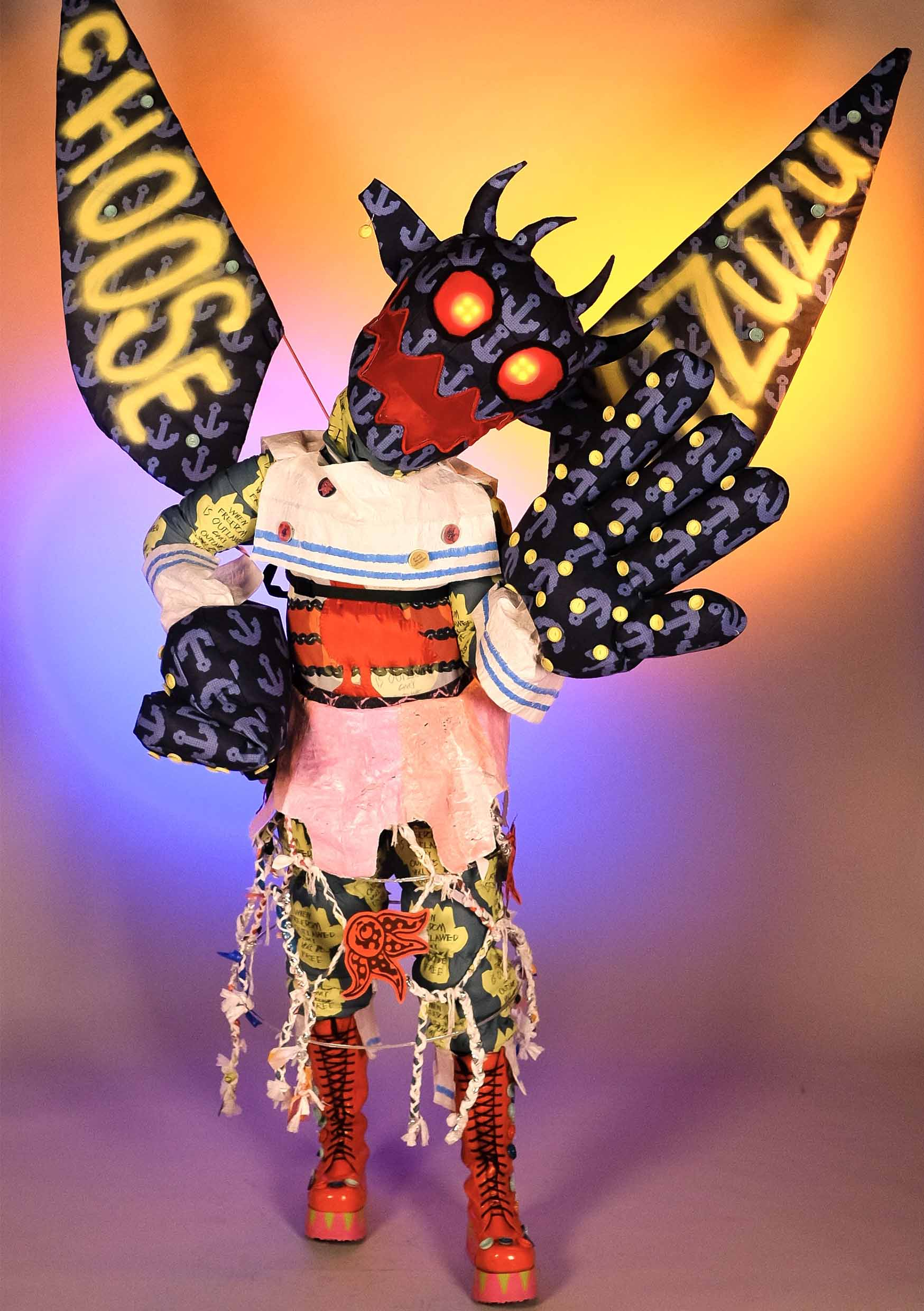 Model wearing Pazuzu costume with blue and orange lighting.