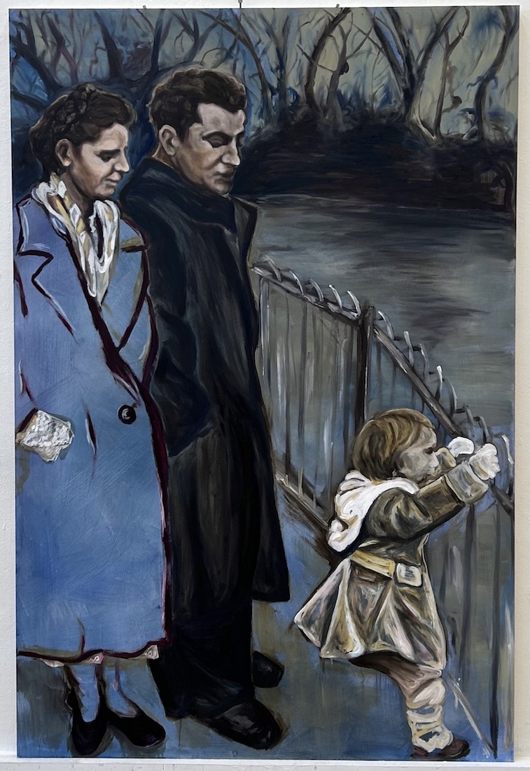 A man and woman walk through a park. The woman is wearing a blue coat. They are standing by a lake. 