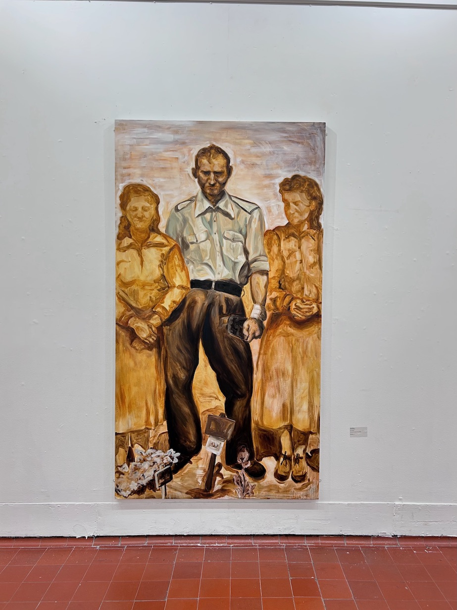 The Partisan: A man stands over a fresh grave with a small wooden marker. He looks down. His eyes cannot be seen. Two women stand either side of him. They are golden, fading into the background yellow hues.