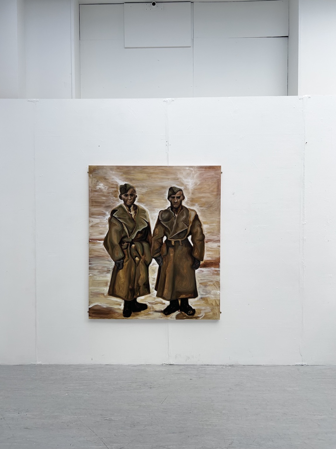 Two coated figures stand in a desert.