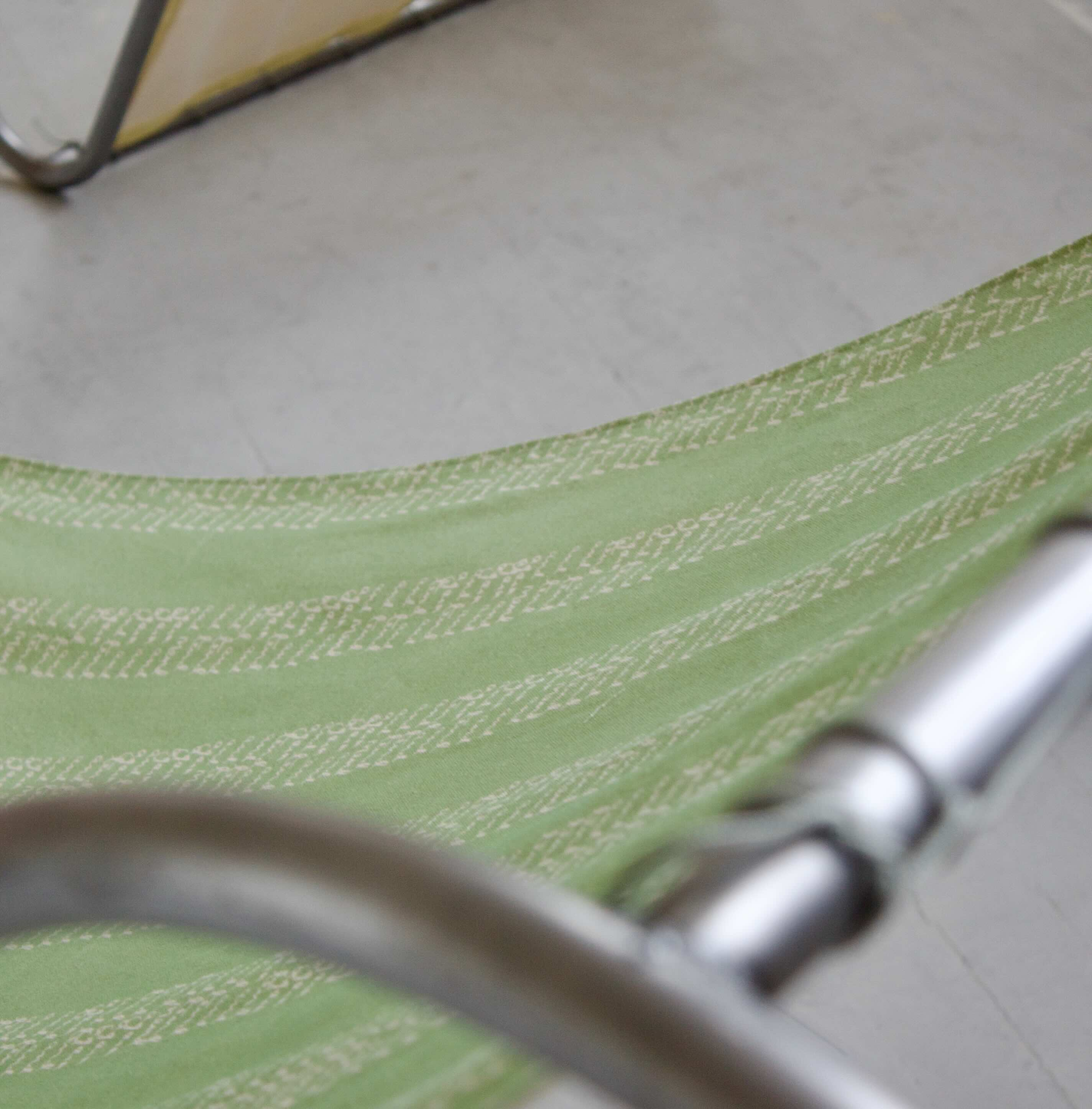 Pictured: close up of a section of the green fabric of the 'd frame', attached to the steel pipe frame by para-cord; there are columns of handwritten cream text printed onto the green fabric.