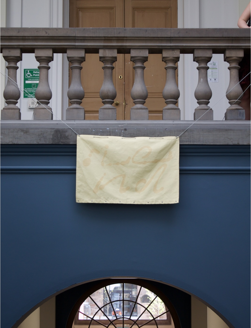 Pictured: yellow fabric with slightly abstracted letter forms that spell 'mend' suspended over the main staircase.