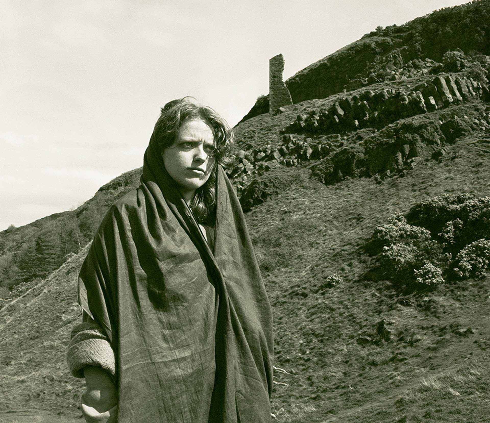 Woman stands infront of mountain range and stone carving