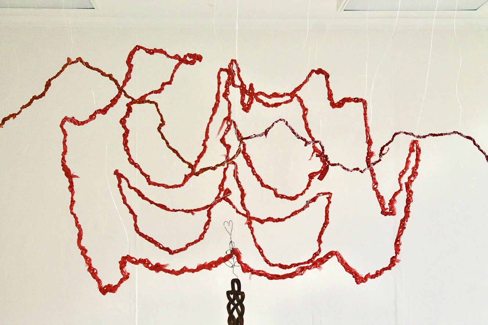 Crochet plastic bags hung to resemble a 3D symbol of a pelvis with a Welsh love spoon hung on the end