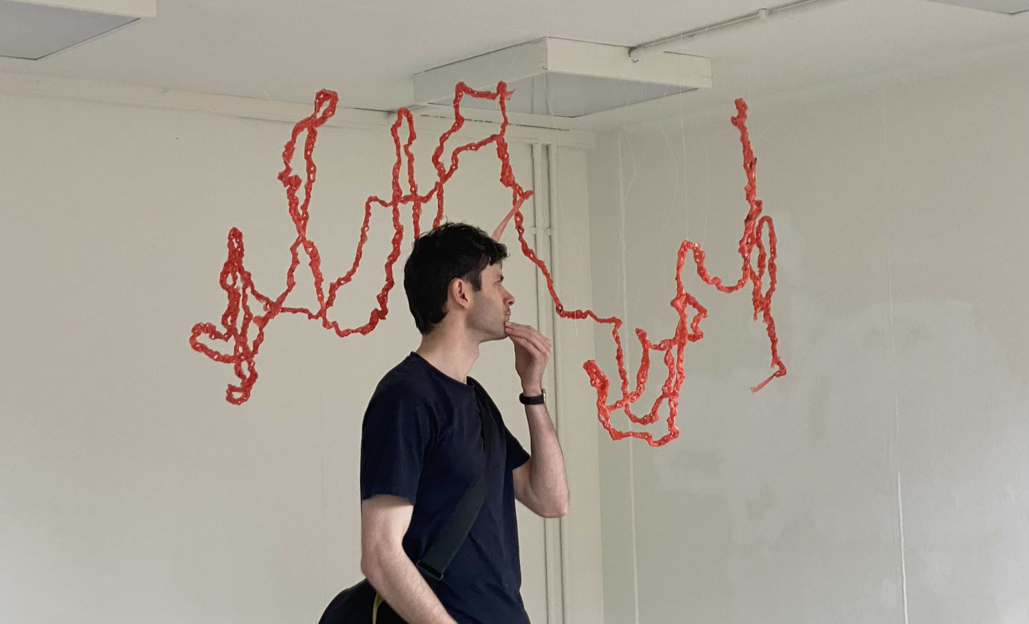 View from the side of crochet plastic bags hung using fishing line with a man looking in a white cube space