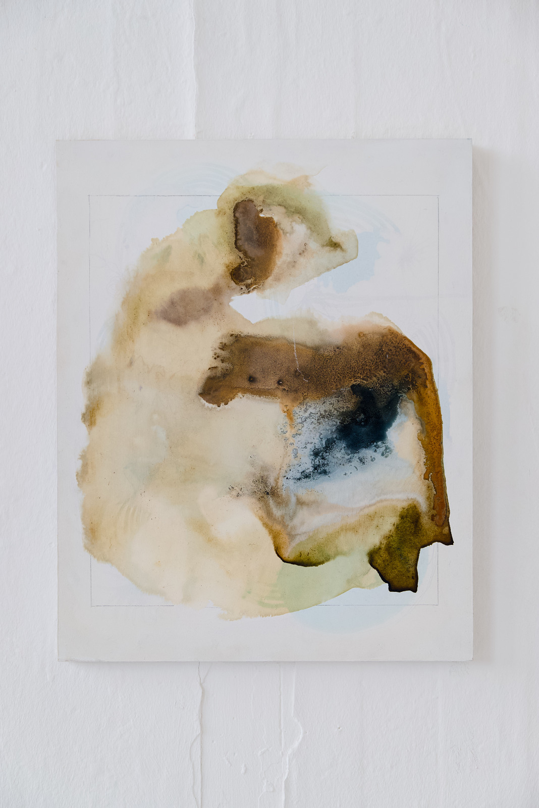 A 40 × 50 cm portrait-format canvas made with natural inks. On a white background, a large irregular stain fills most of the centre of the canvas, contained loosely within a faint rectangular outline. The colours are mostly pale cream, beige, ochre, brown, soft green, and light blue, with a darker blue-black area near the right centre. The inks spread in translucent layers, with soft bleeding edges, sedimented brown patches, tide marks, and darker crystallised areas along the right side and lower edge.