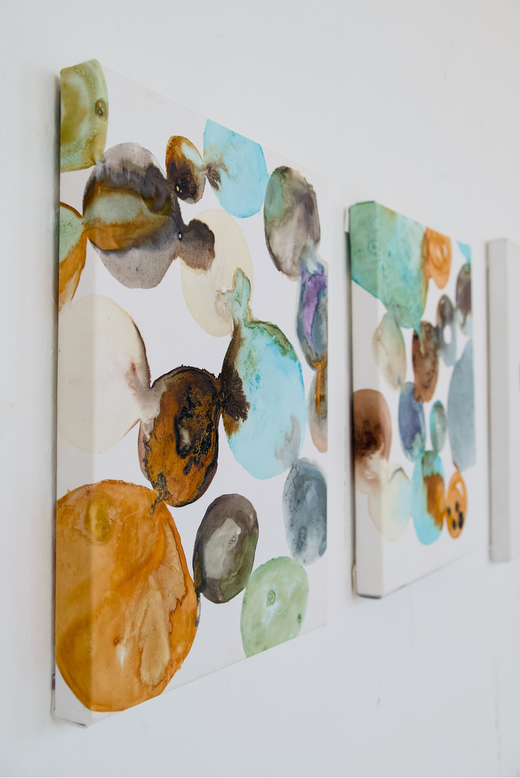 A 40 × 50 cm portrait-format canvas made with natural inks. On a white background, multiple rounded pools of colour are arranged across the surface, some cropped by the canvas edges. The colours include pale turquoise, soft green, orange, rust brown, grey, black, cream, and purple. Several forms overlap and bleed into each other, creating translucent washes, dark sedimented patches, tide marks, crystallised edges, and small circular areas where pigment has concentrated.