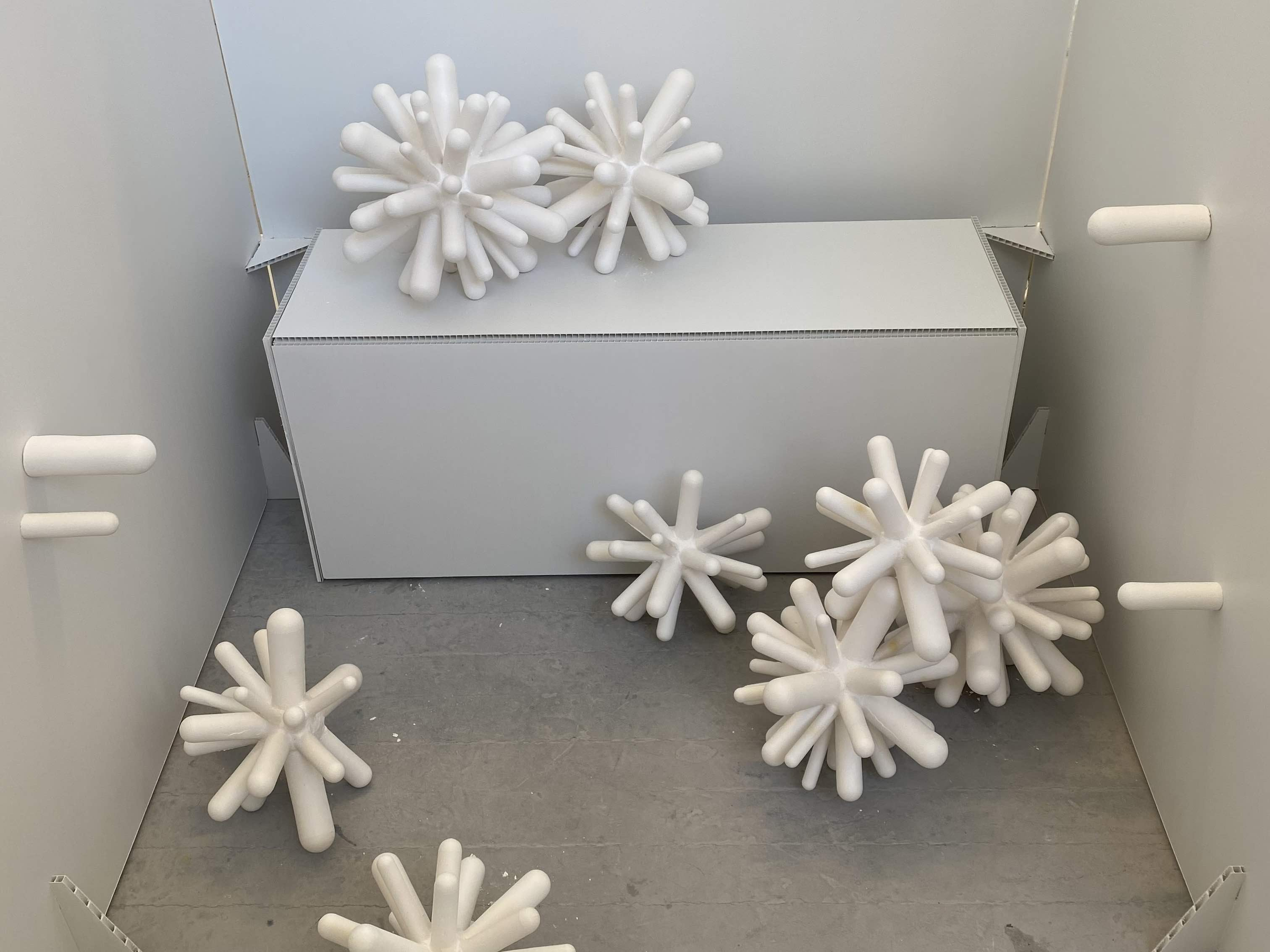 Atomic shaped sculptures falling from plinth onto floor.