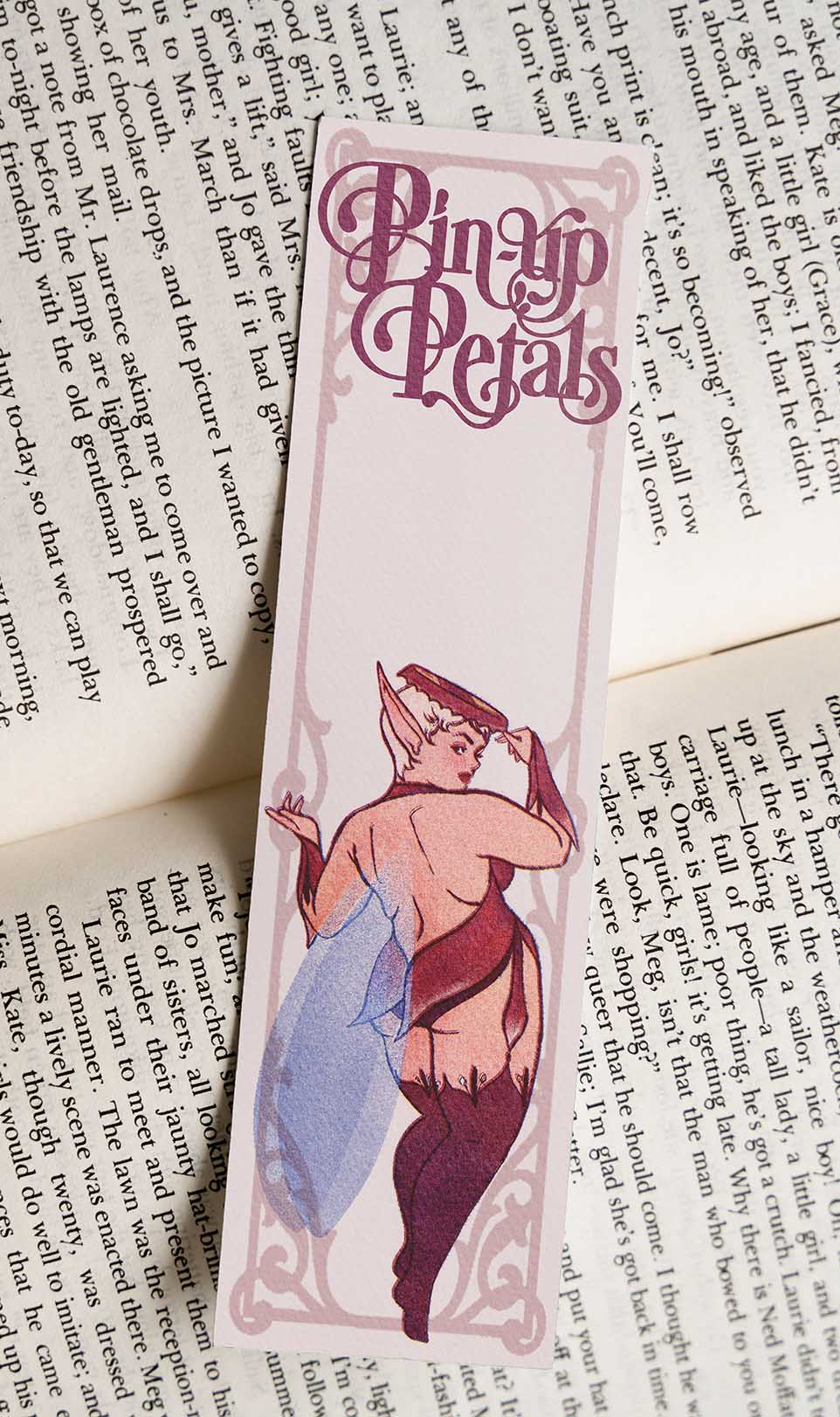 A pink bookmark with a pin-up style fairy wearing a bottle cap hat. 