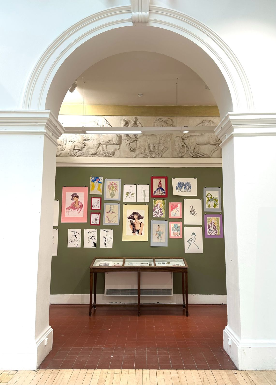 drawings displayed on a green wall in the ECA, through a white arch