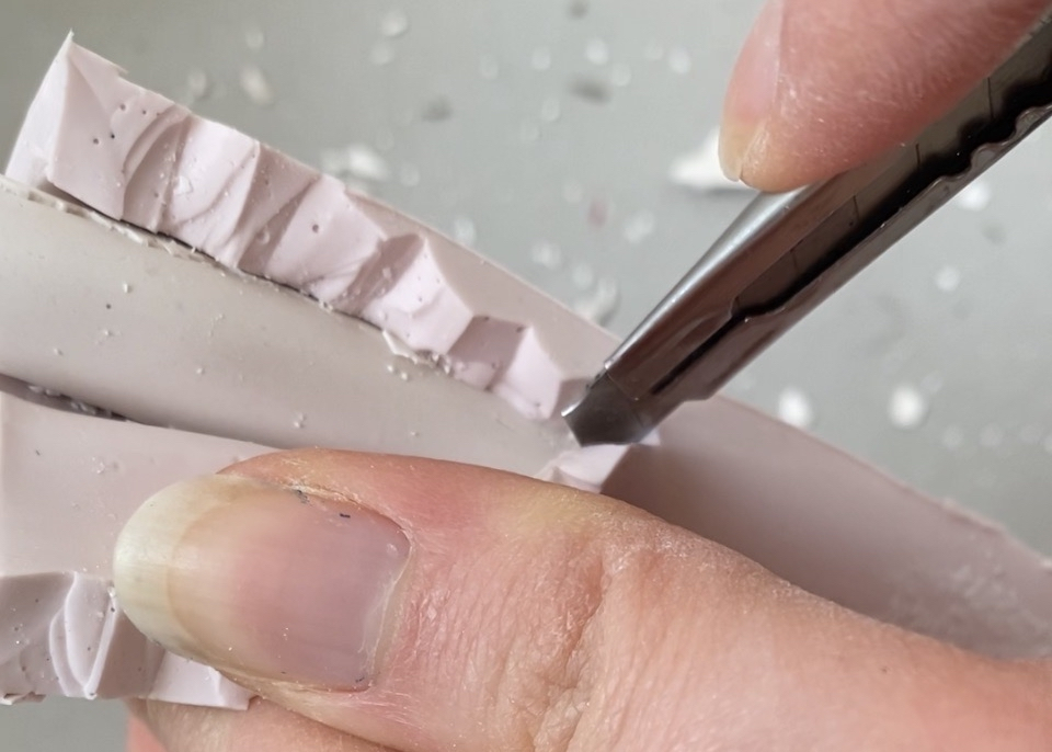 Video still of artist's hands cutting open a pink silicone dilator mould.