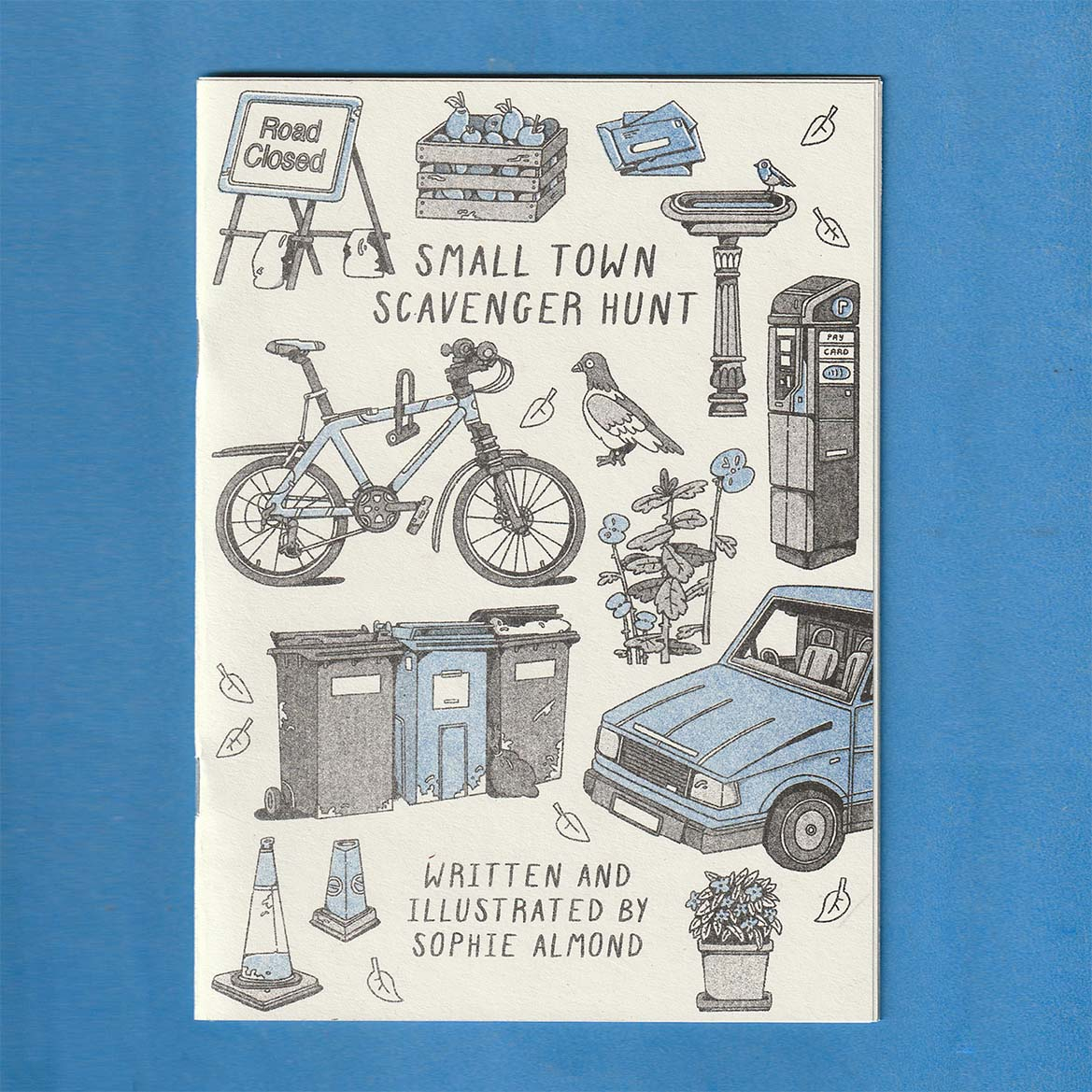 front cover of a risograph printed zine titled 'small town scavenger hunt' featuring several objects seen in a small town such as a car, bike, pigeon, and bins. printed with blue and black riso ink
