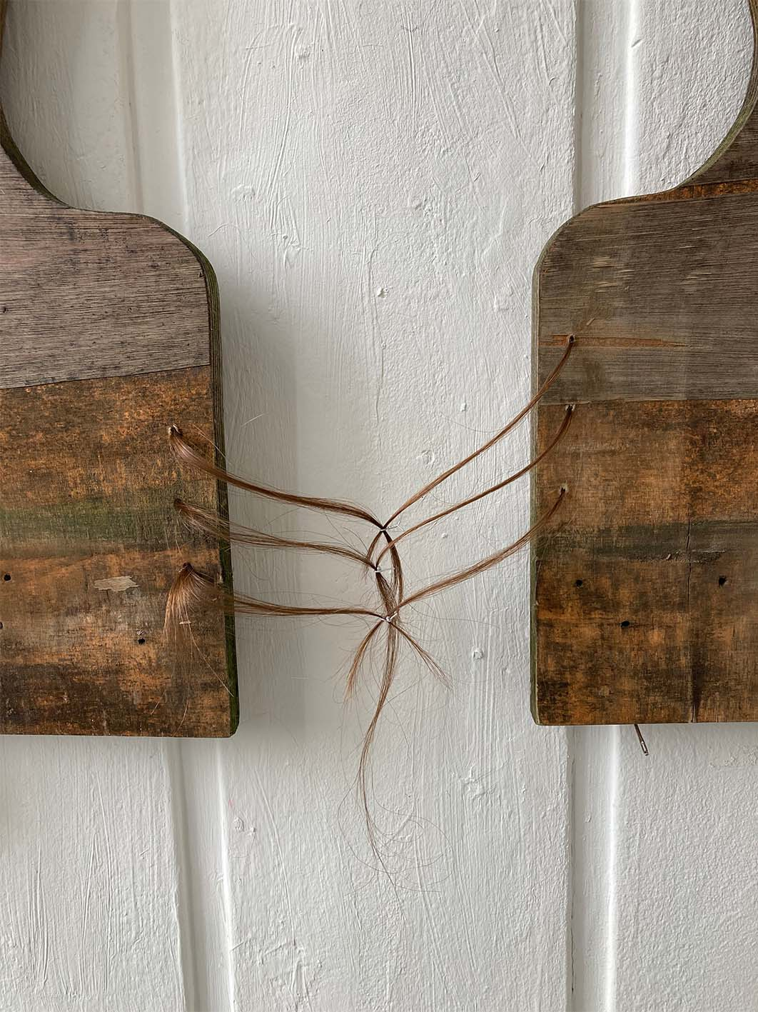 Image of wooden sculpture installed onto wall using sewing needles, with hair binding.