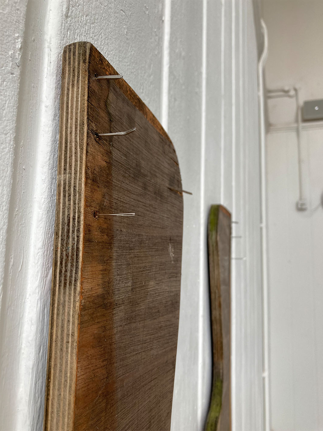 Image of wooden sculpture installed onto wall using sewing needles, close up.