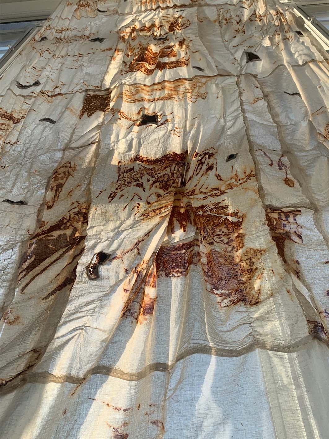Image of cotton textile dyed with rust installed over window.