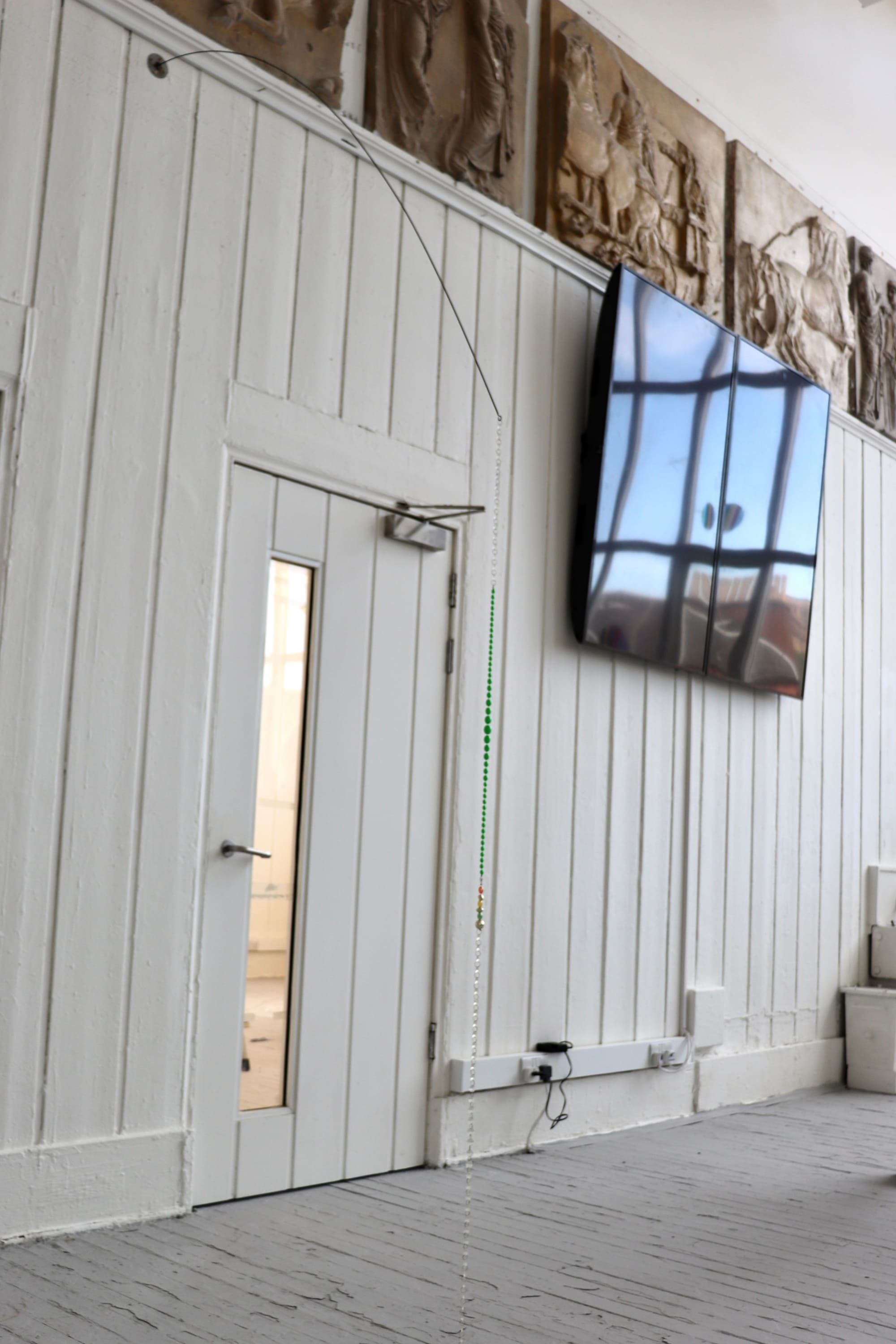 a beaded sculpture hanging from an iron rod at the top of the wall
