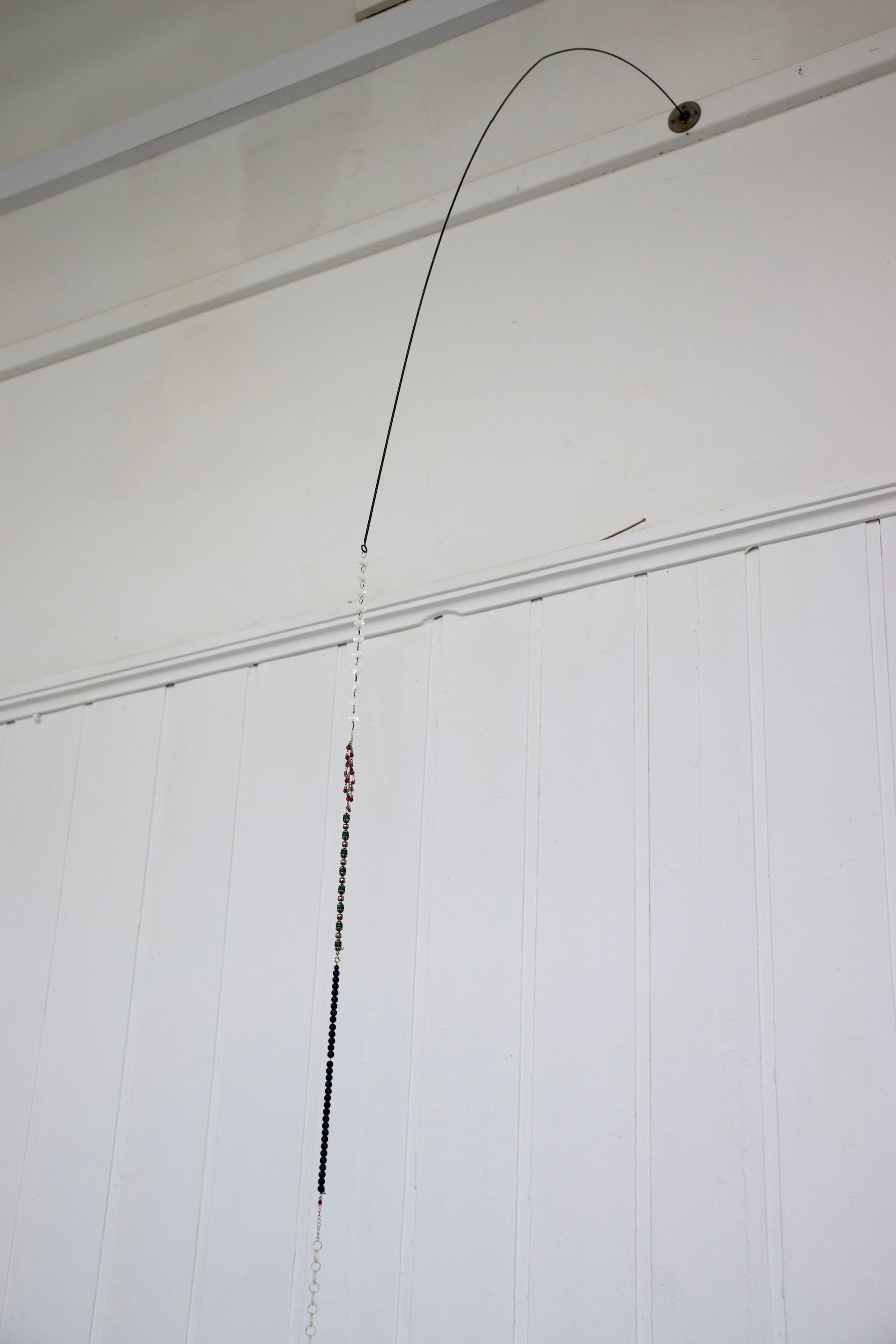 a beaded sculpture hanging from an iron rod at the top of the wall