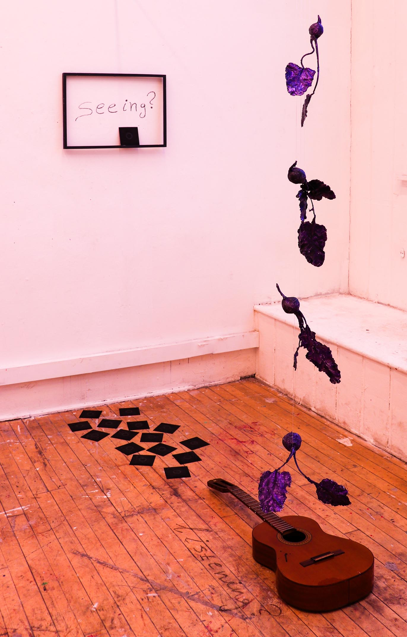 Installation of purple cast beetroot sculptures suspended above a guitar lying on a wooden floor.